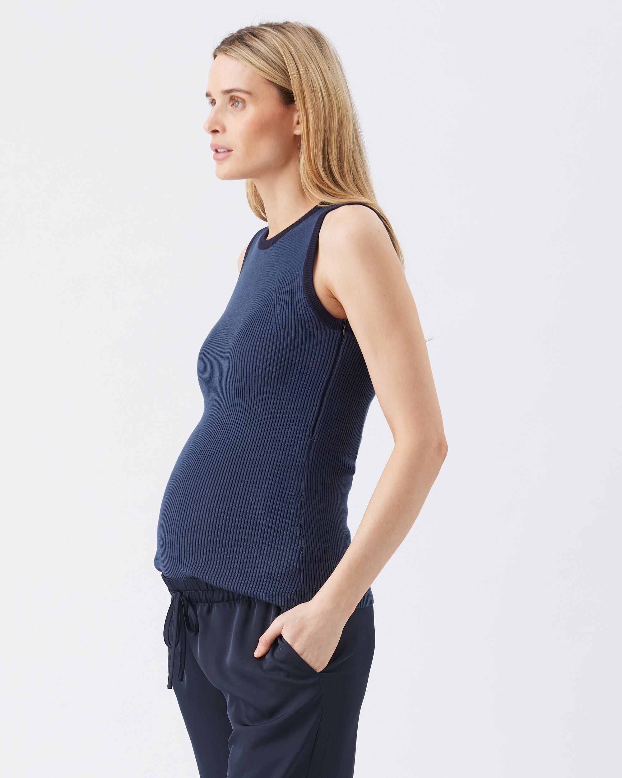 Side view of a pregnant woman wearing a navy blue sleeveless top and pants on a white background