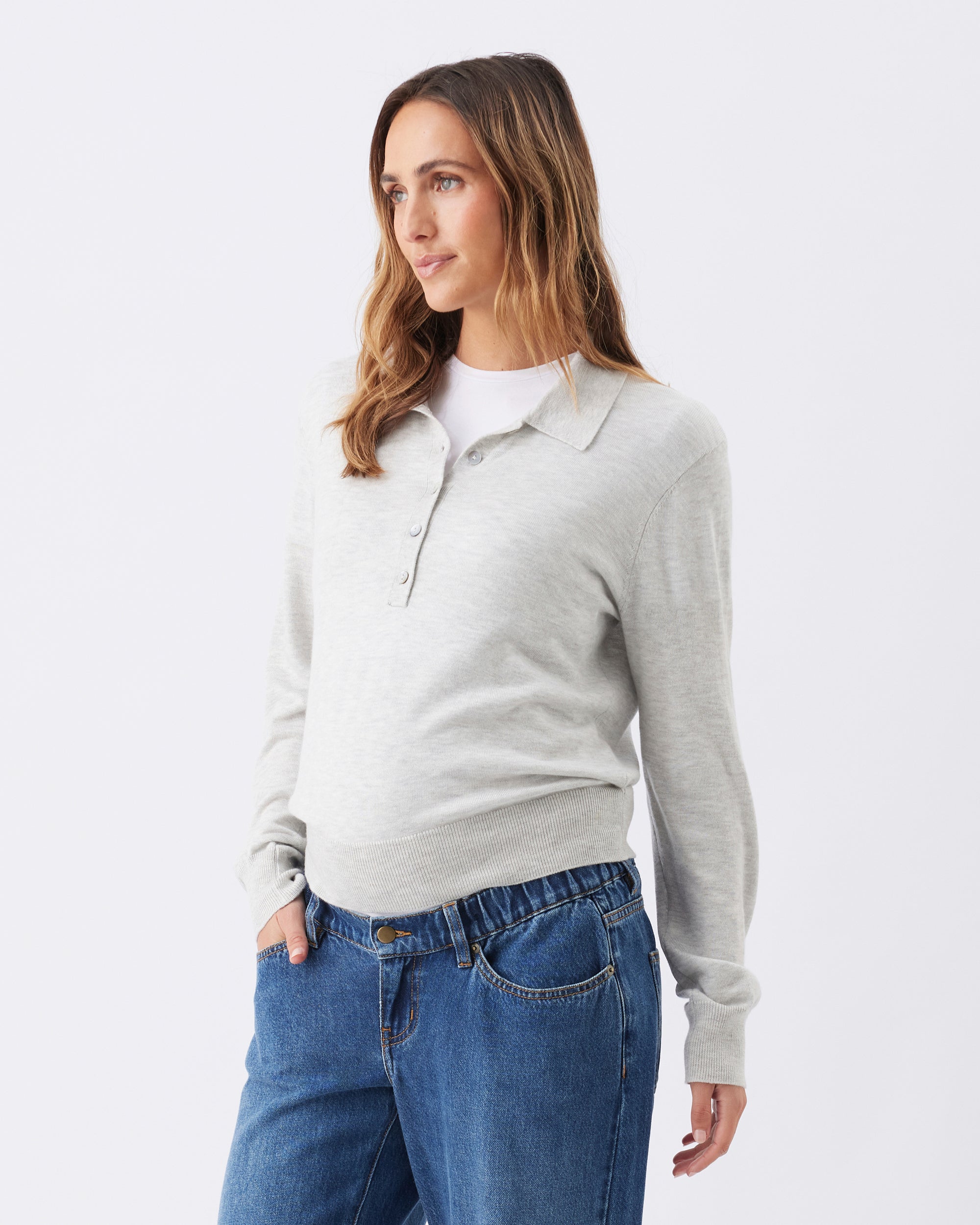 Side view of a pregant woman wearing a light gray sweater and blue jeans on a white background