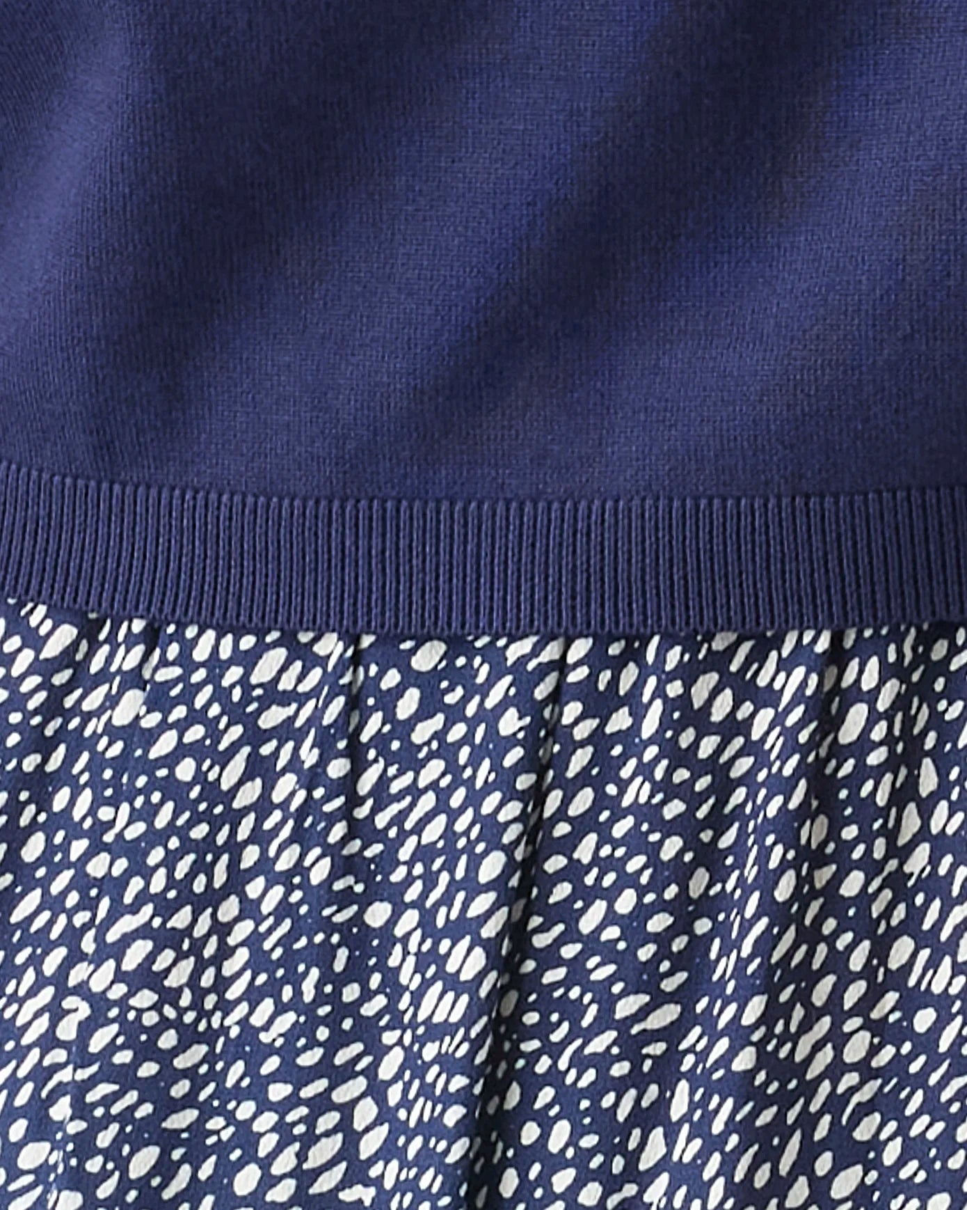 Close-up of a navy blue knit top with a ribbed hem and a matching navy and white spotted print skirt or lower section.