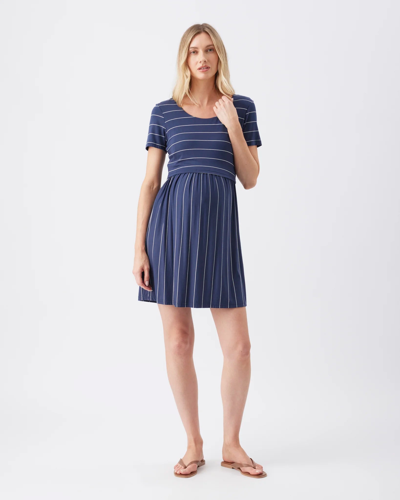 A woman modeling a short-sleeve babydoll dress with navy blue and white stripes, standing against a plain white studio background.