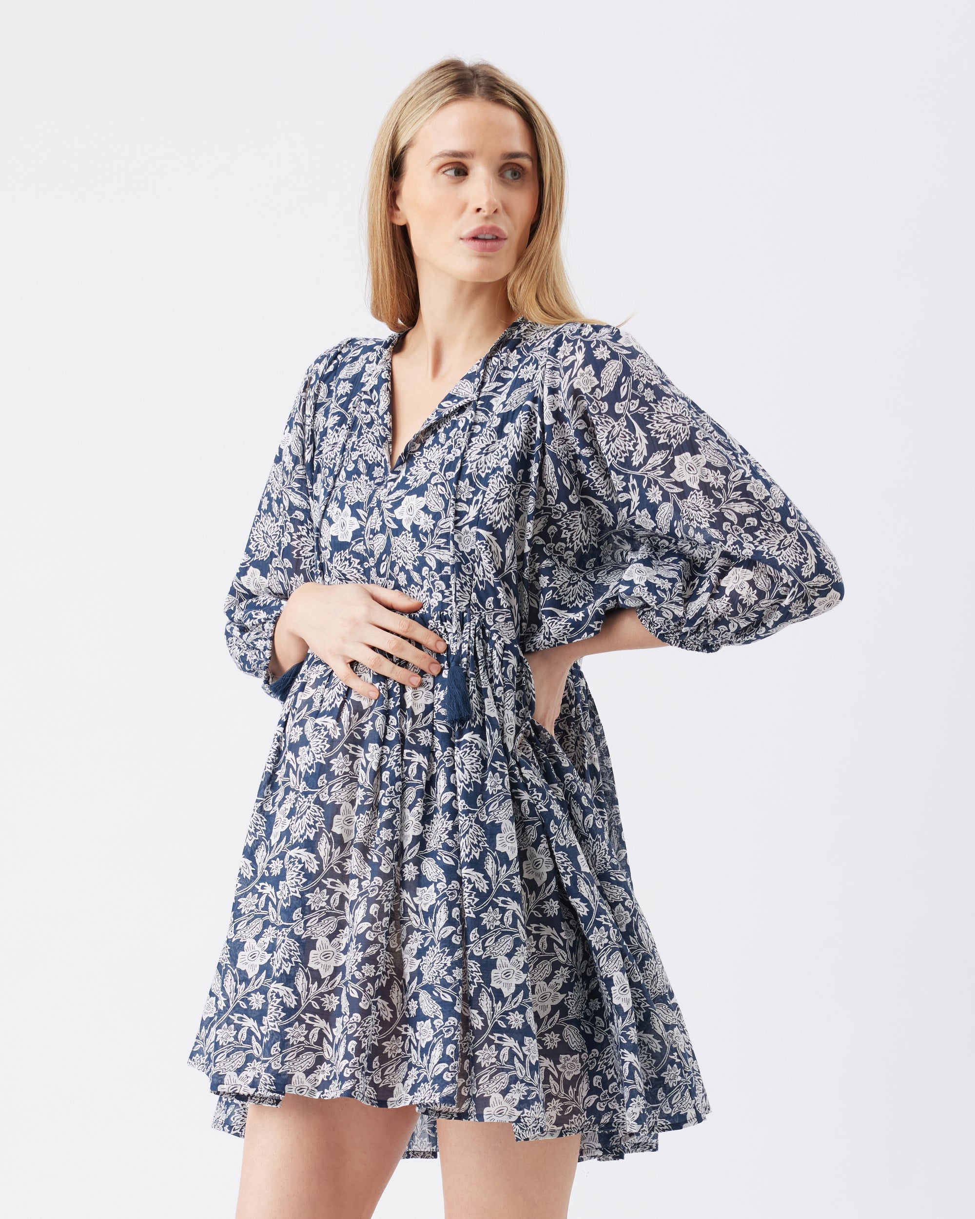 Side view of a pregnant woman wearing a blue floral dress on a white background