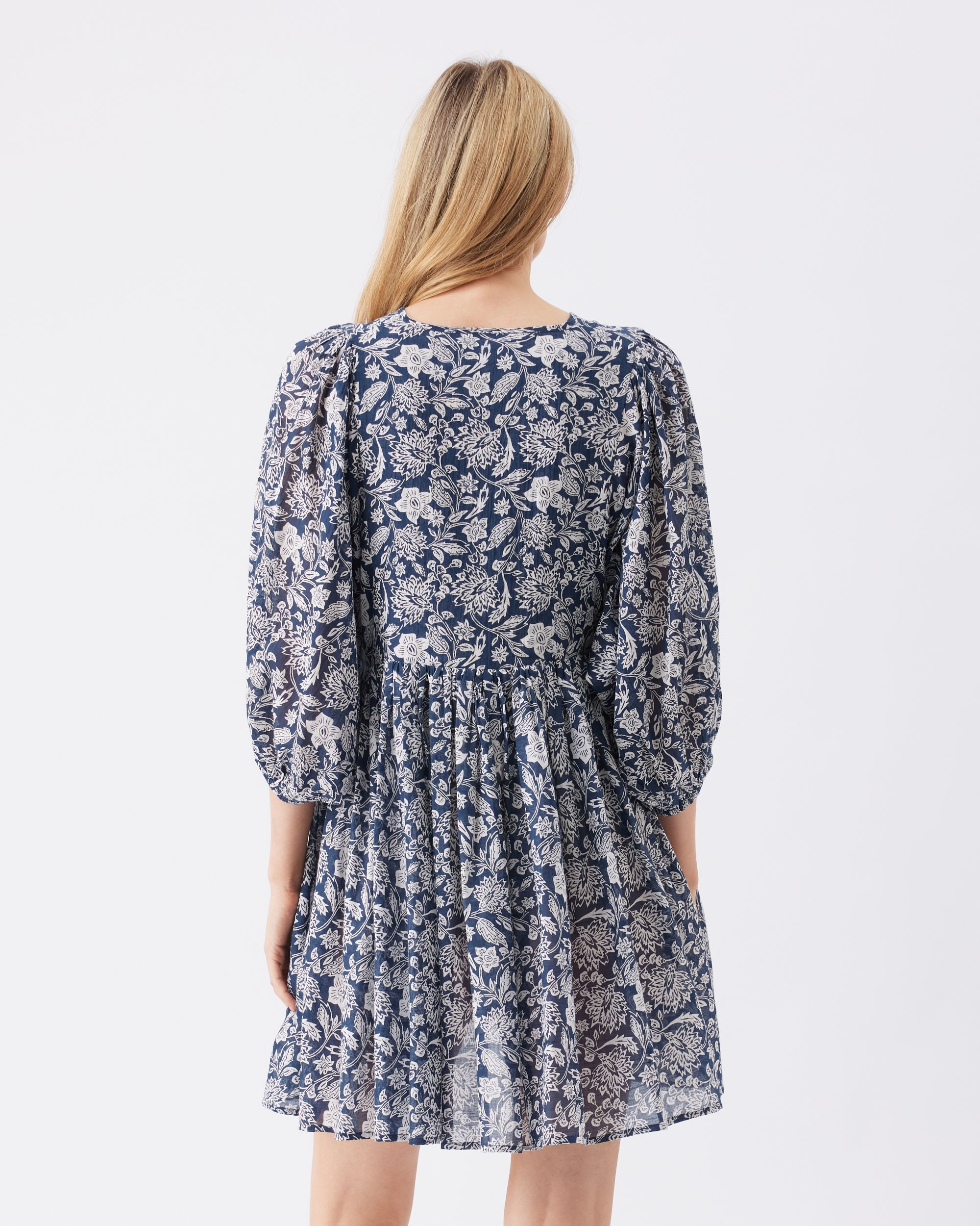 Back view of a woman wearing a blue floral dress on a white background