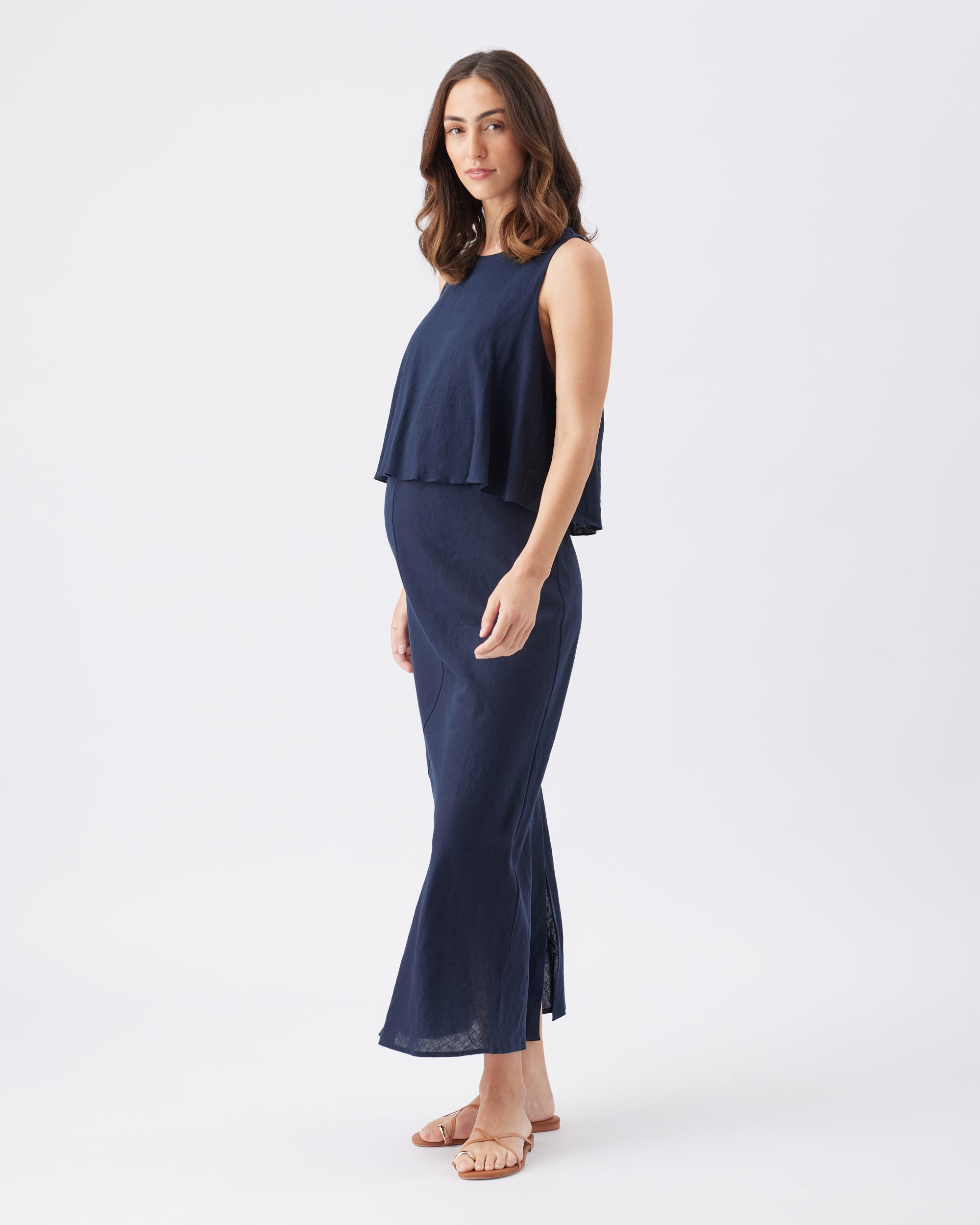 Side view of a pregnant woman wearing a navy blue sleeveless maxi dress on a white background