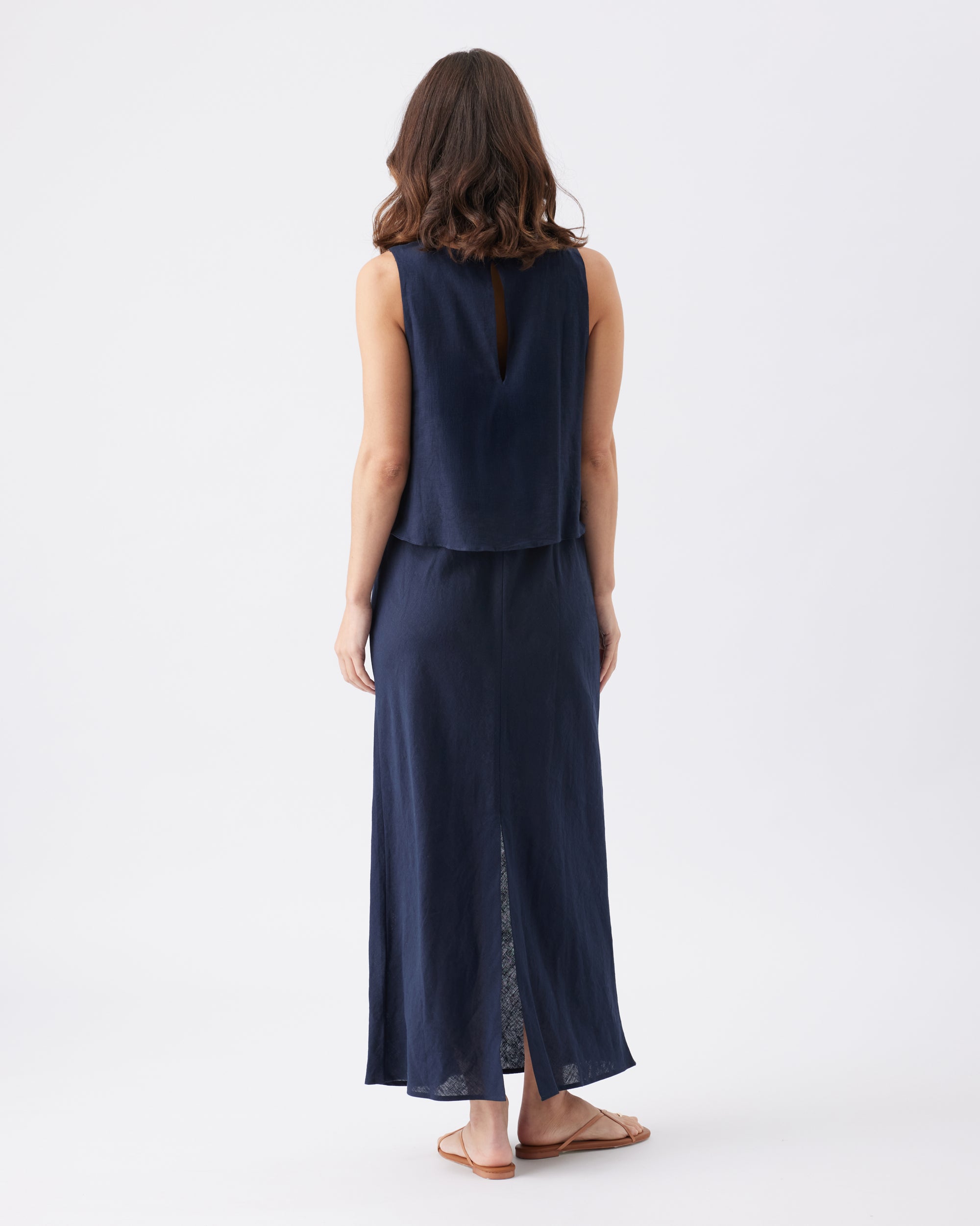 Back view of a woman wearing a navy blue sleeveless maxi dress on a white background