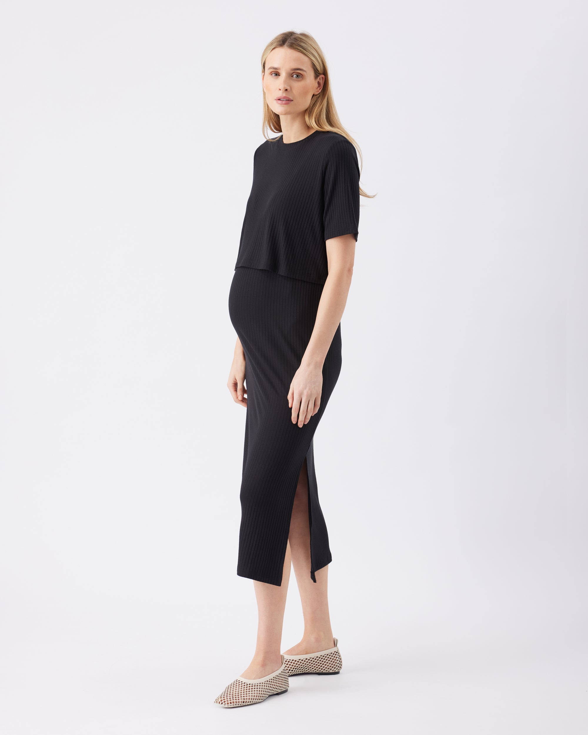 Side view of a pregnant woman wearing a black dress with a side split on a white background