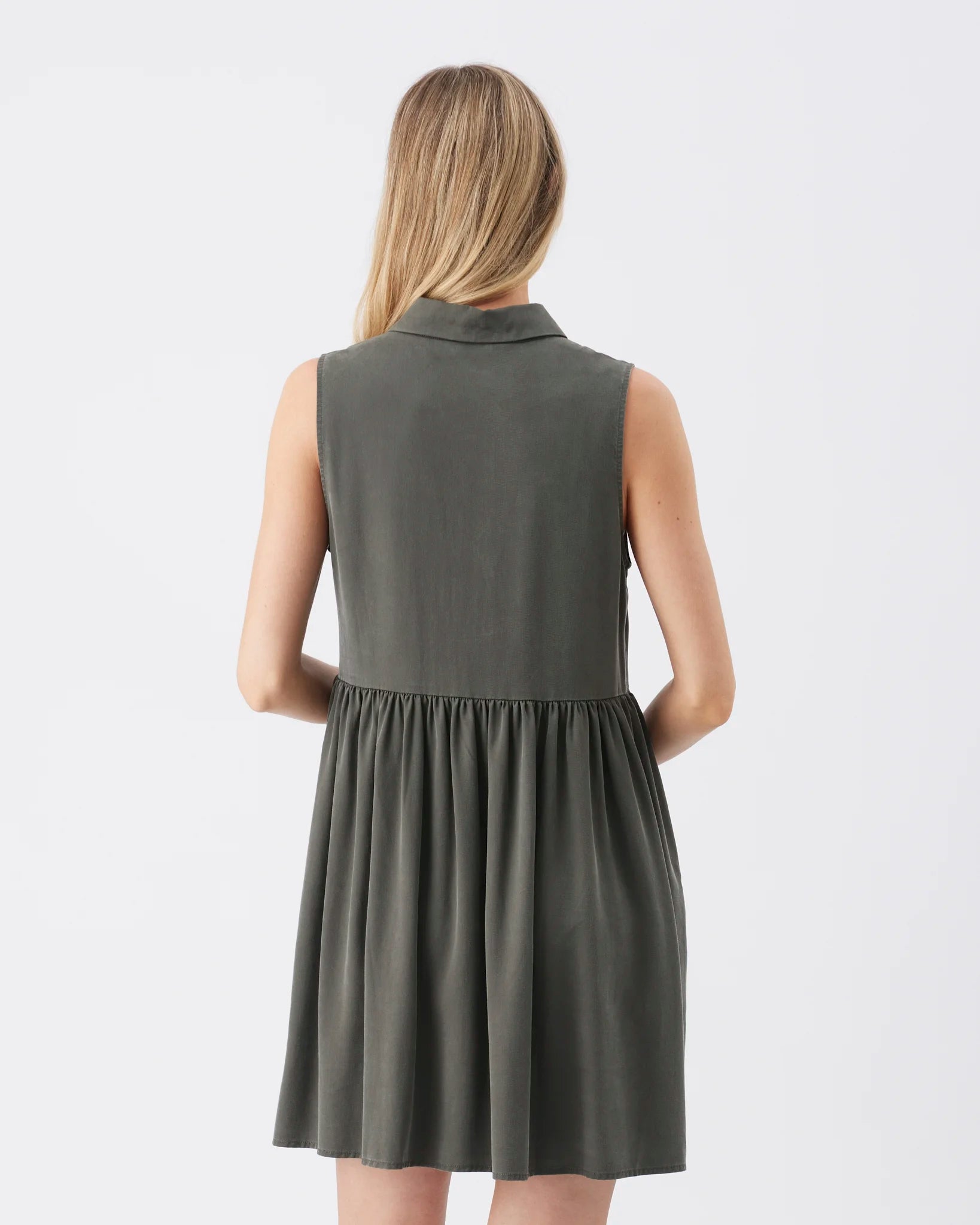 A woman viewed from the back wearing a sleeveless dark gray dress with a collar and gathered waist, against a plain light gray studio background.