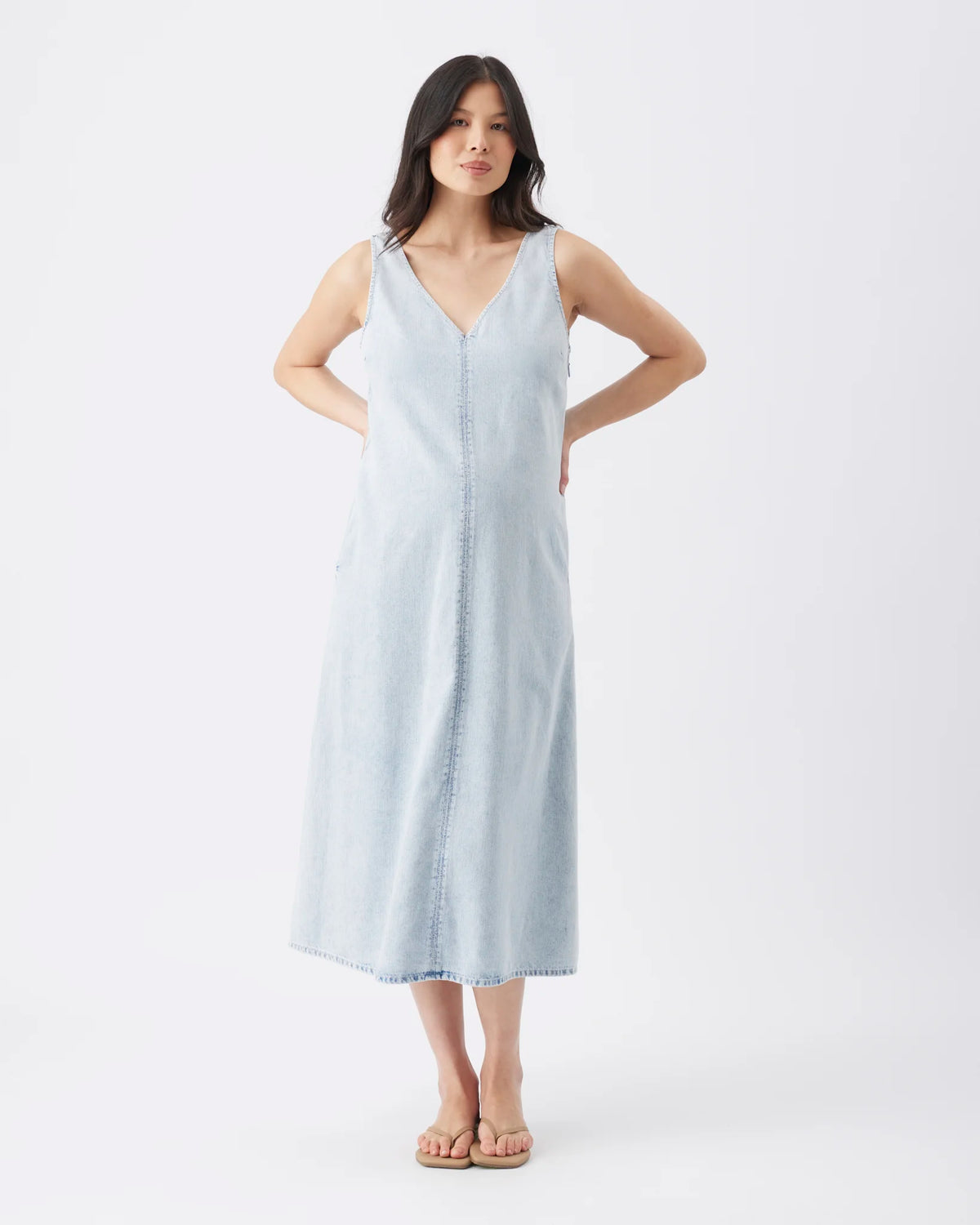 A woman modeling a light blue sleeveless midi dress with a V-neckline and front button placket, standing against a plain white studio background.