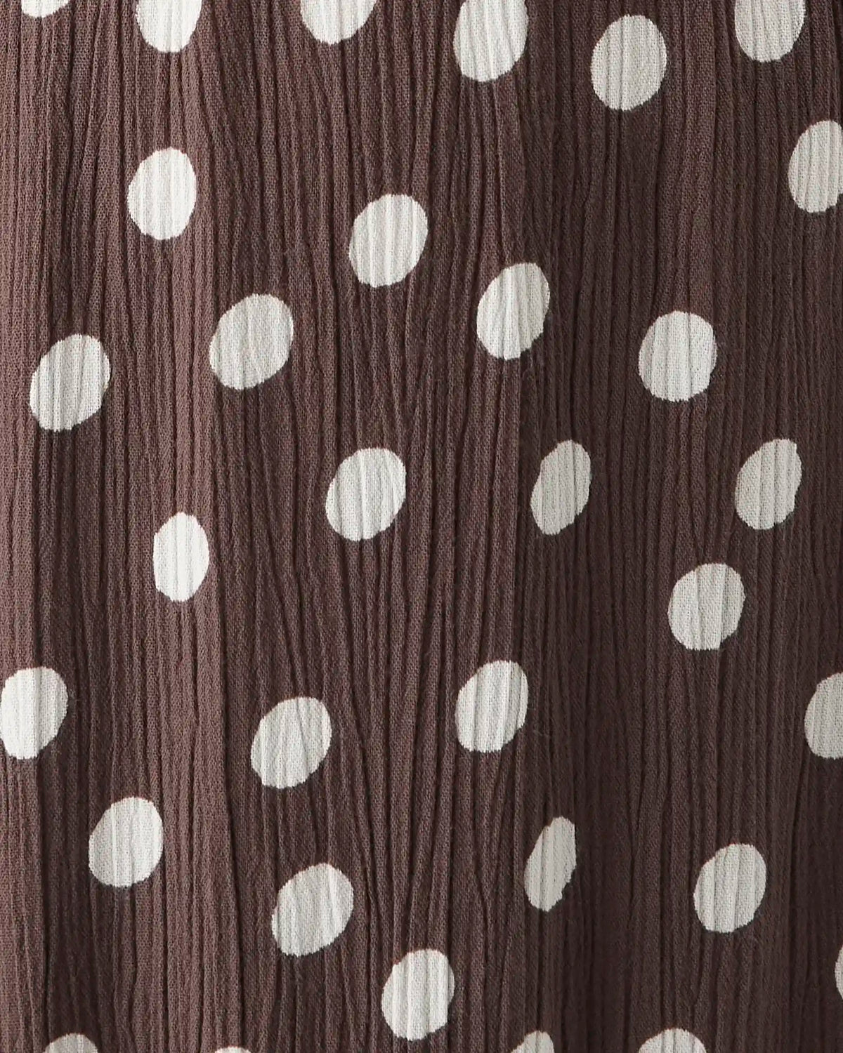 A close-up of a crinkled fabric with a dark brown base and a pattern of large white polka dots.