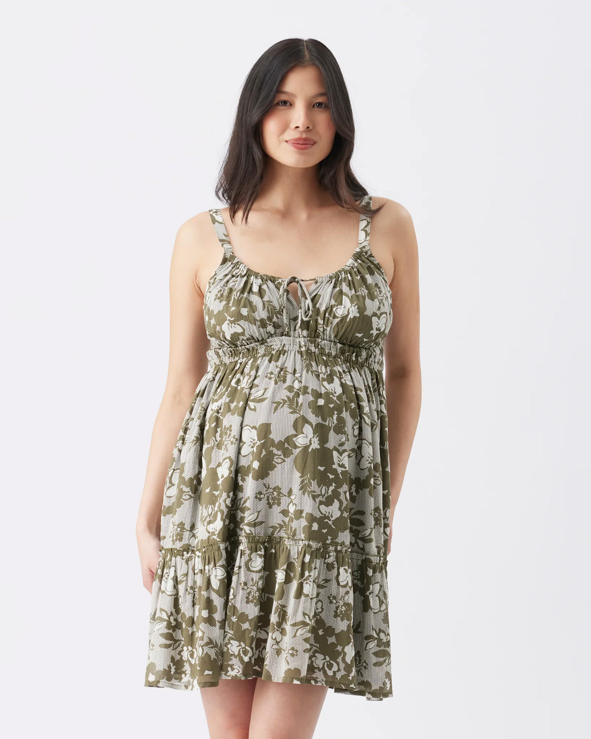 A woman modeling a sleeveless tiered dress with a green and beige abstract floral print against a plain white studio background.