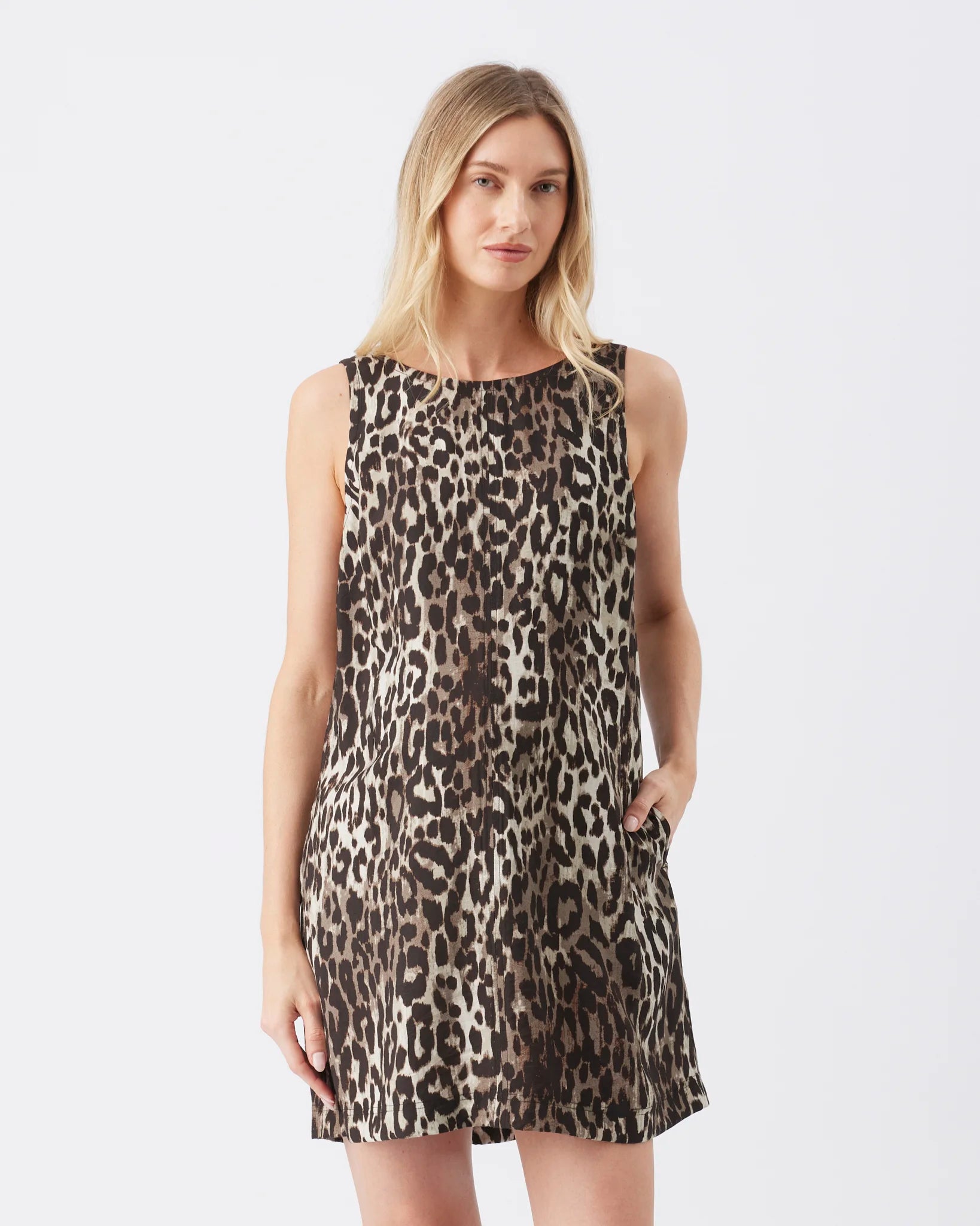 A woman modeling a sleeveless leopard-print dress with a gathered neckline and side pockets, photographed against a plain light gray studio background.