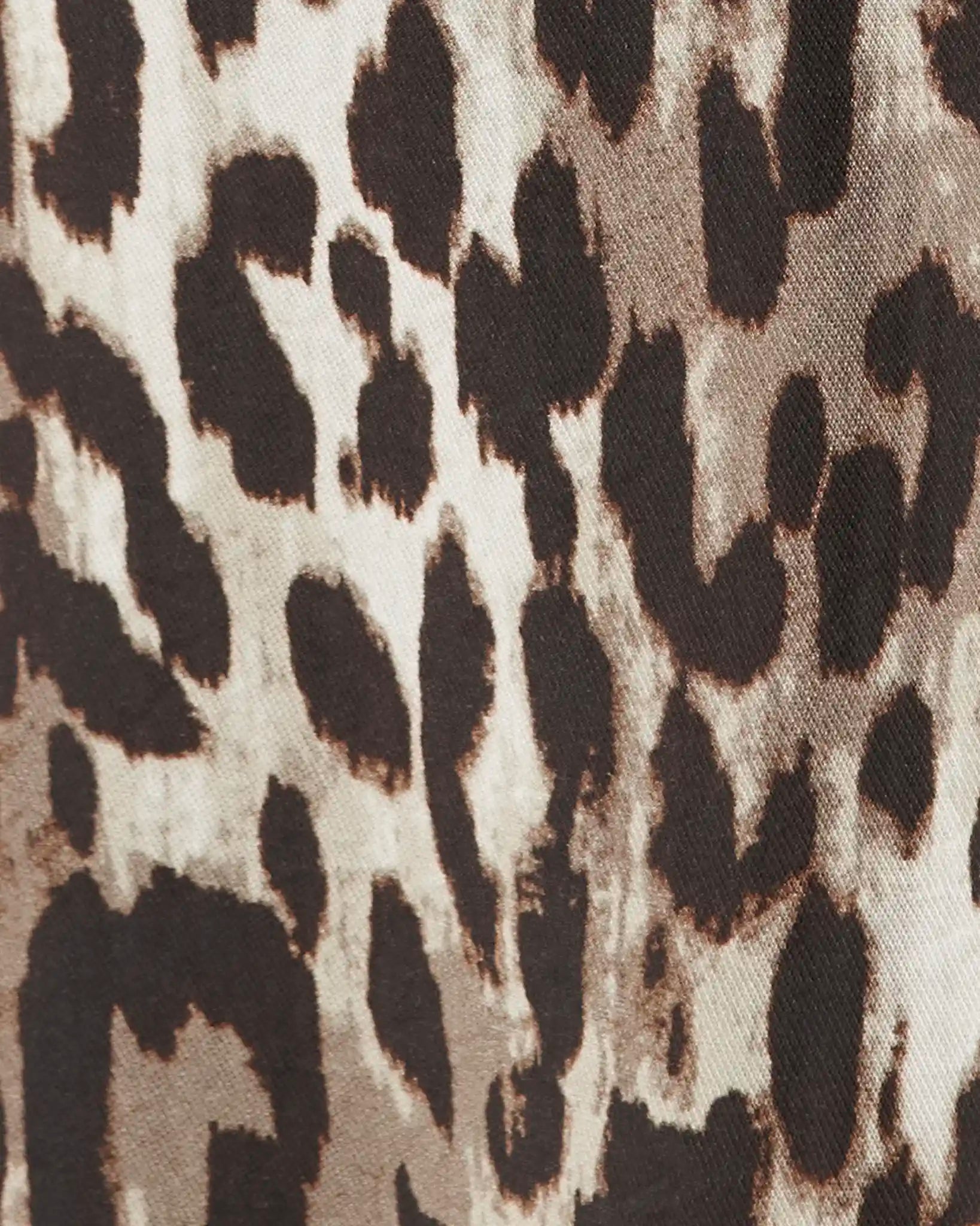 Close-up of a leopard print fabric pattern with dark brown and black spots on a warm beige background.
