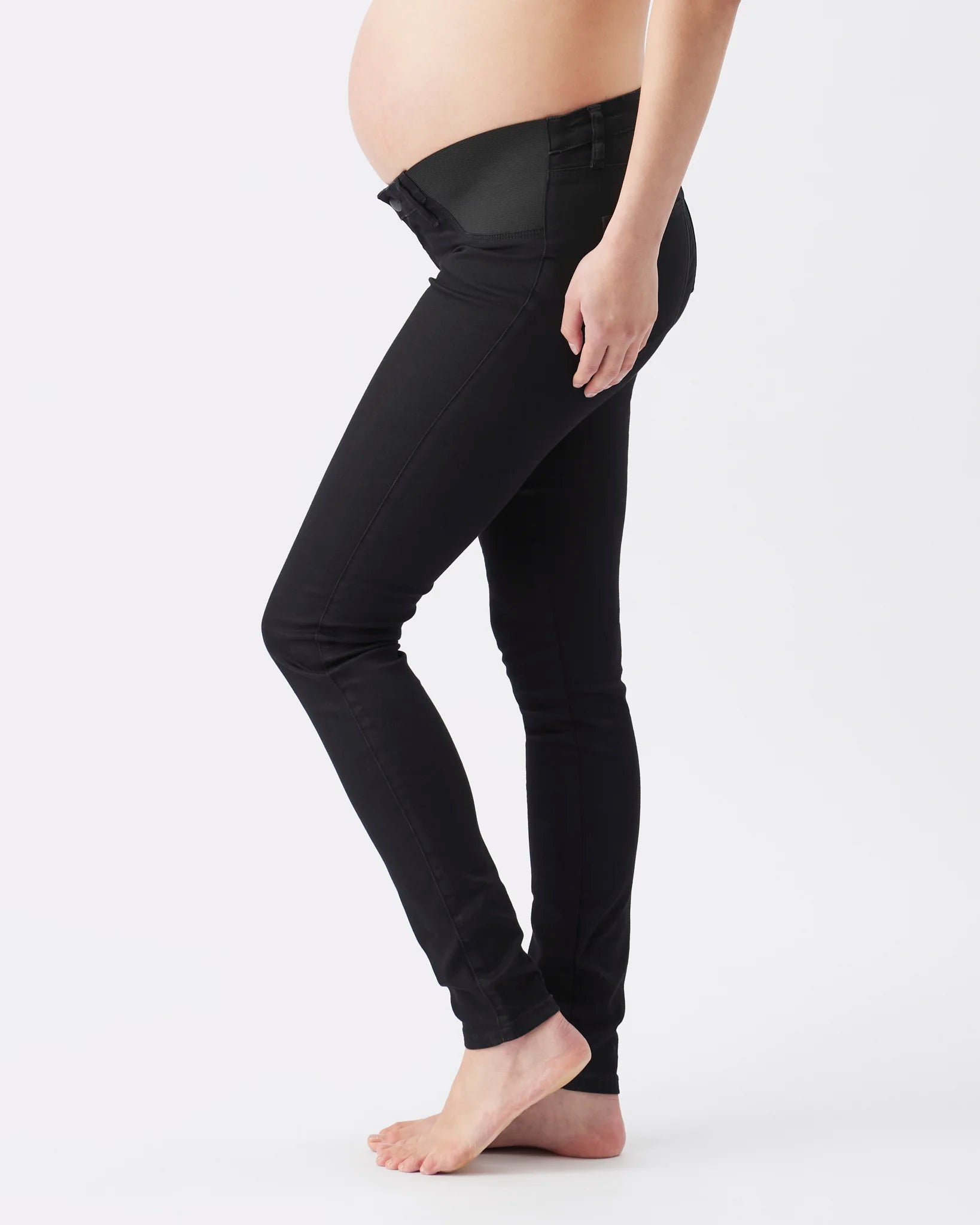 Black maternity leggings with a sheer mesh panel at the waistband, shown on a pregnant model from the side against a light gray background.