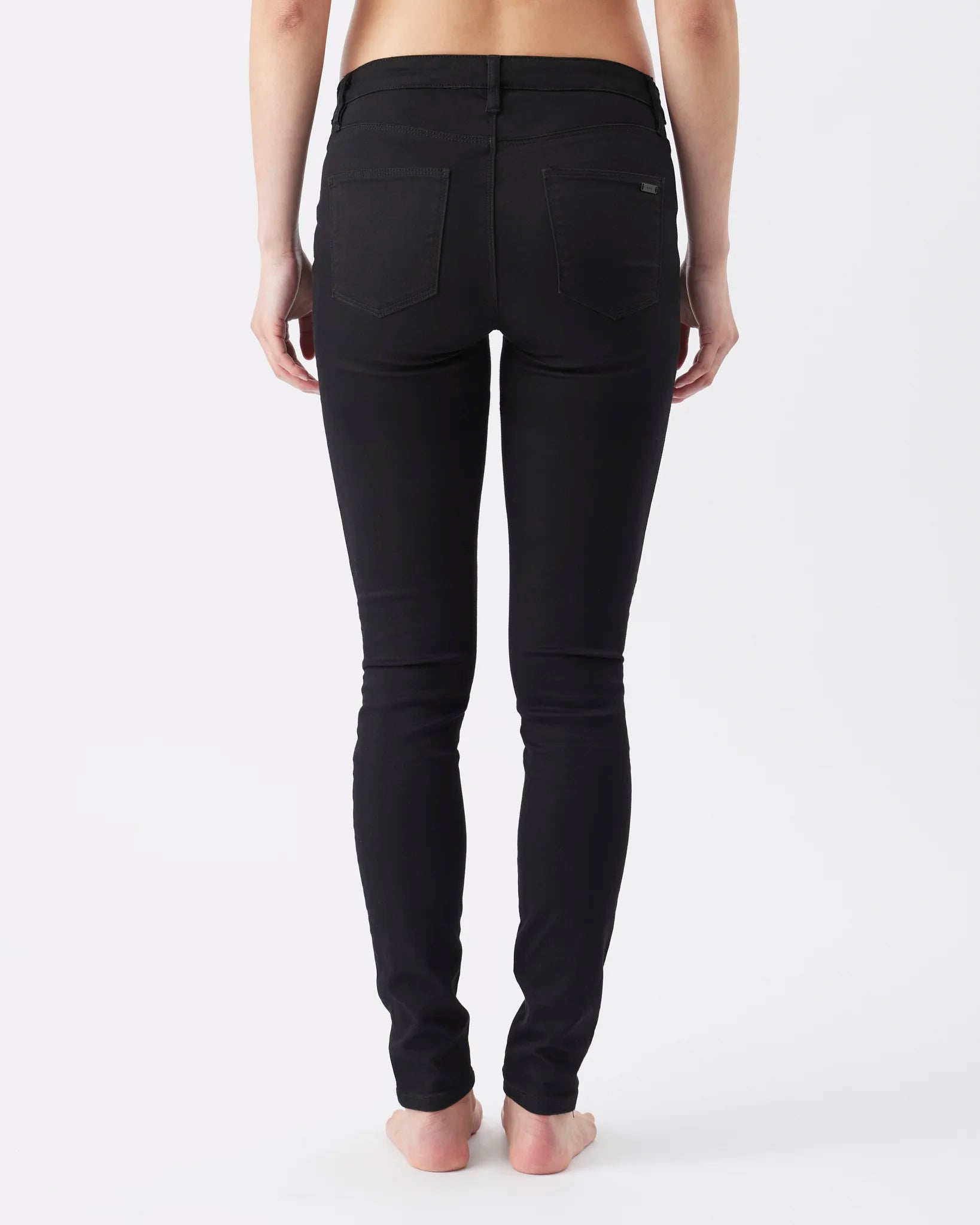 Rear view of a model wearing black skinny jeans against a plain white studio background.