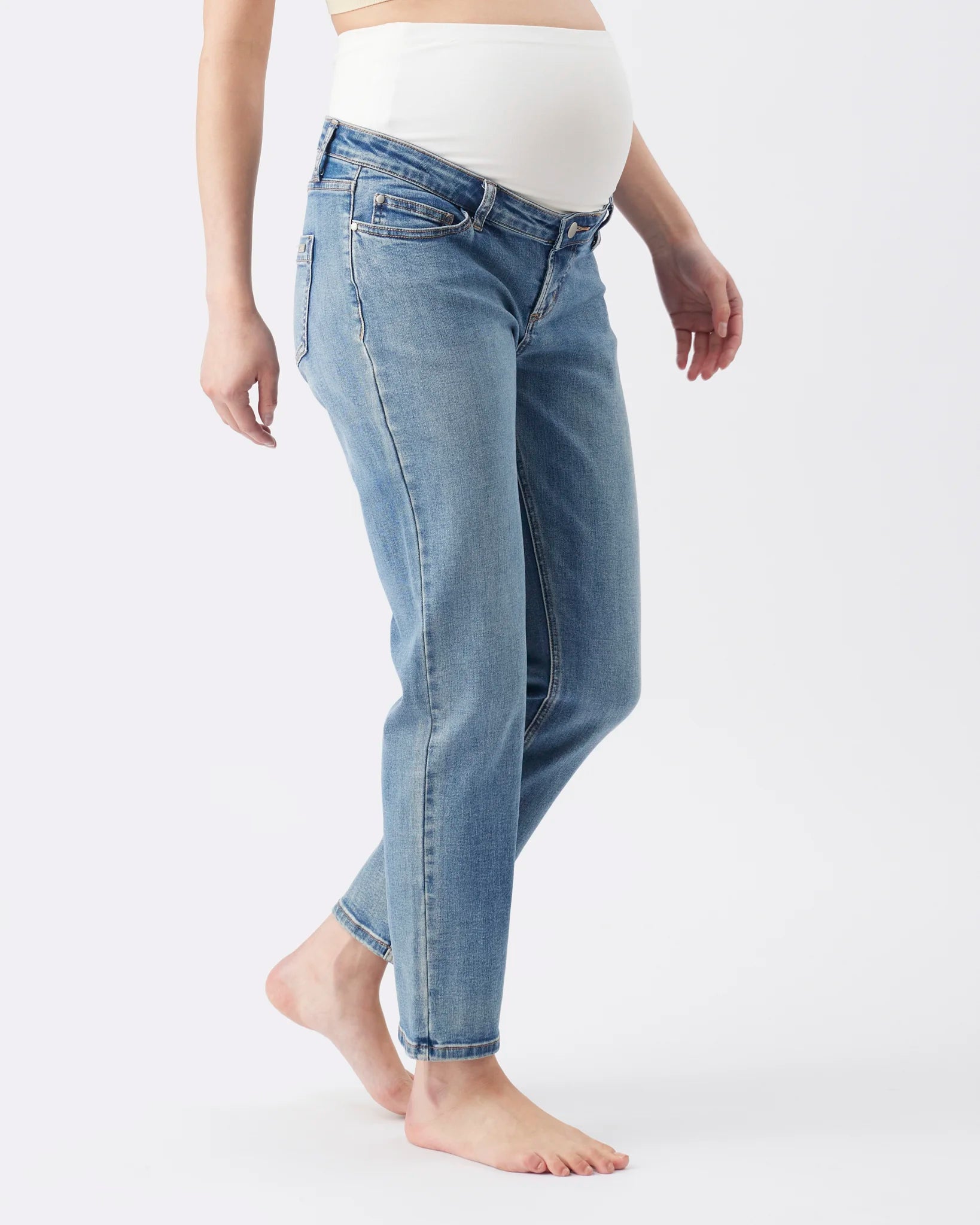 A pregnant model wearing light blue maternity jeans and a white maternity top, shown from the waist down against a plain white studio background.