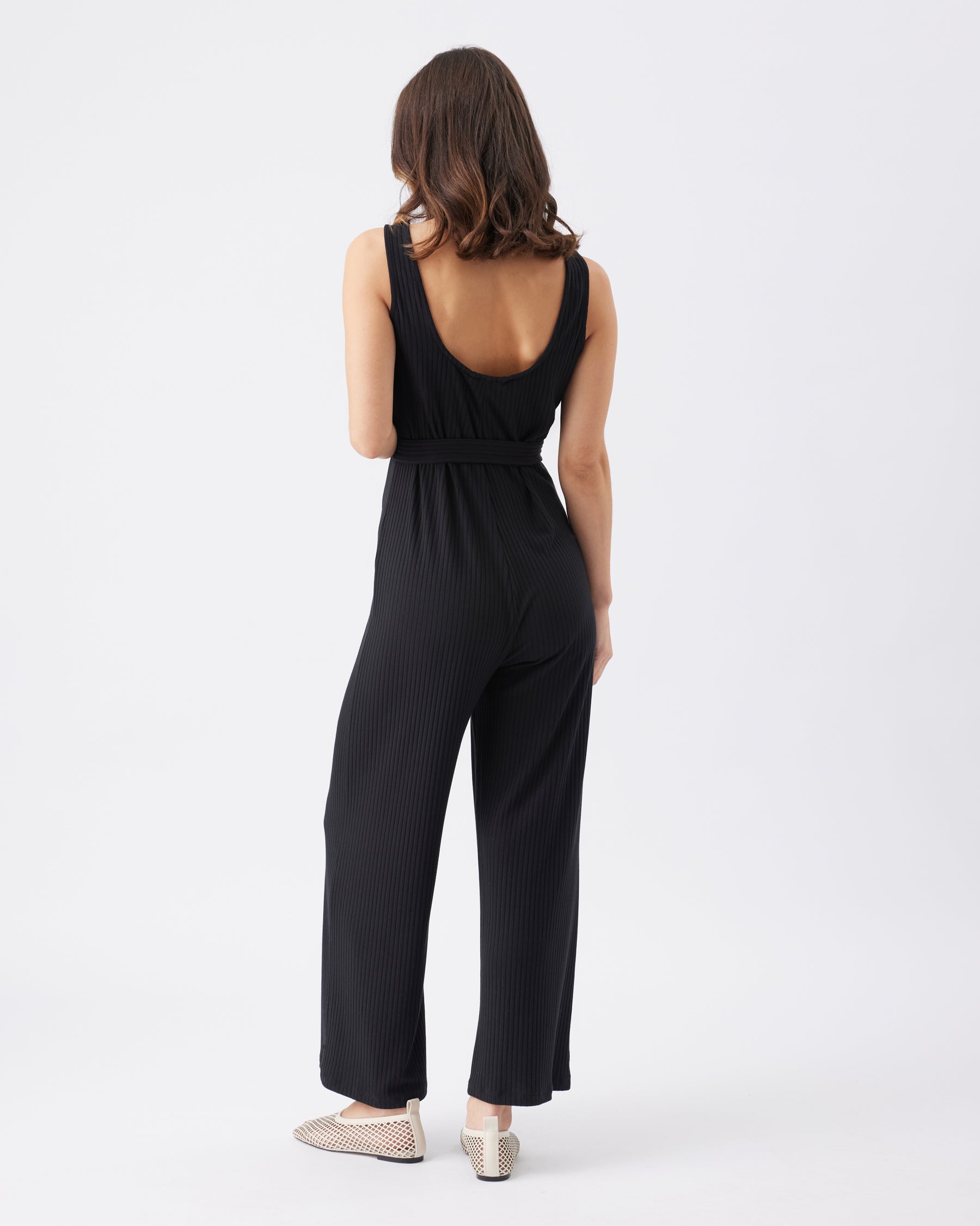 Back view of a woman wearing a black jumpsuit on a white background