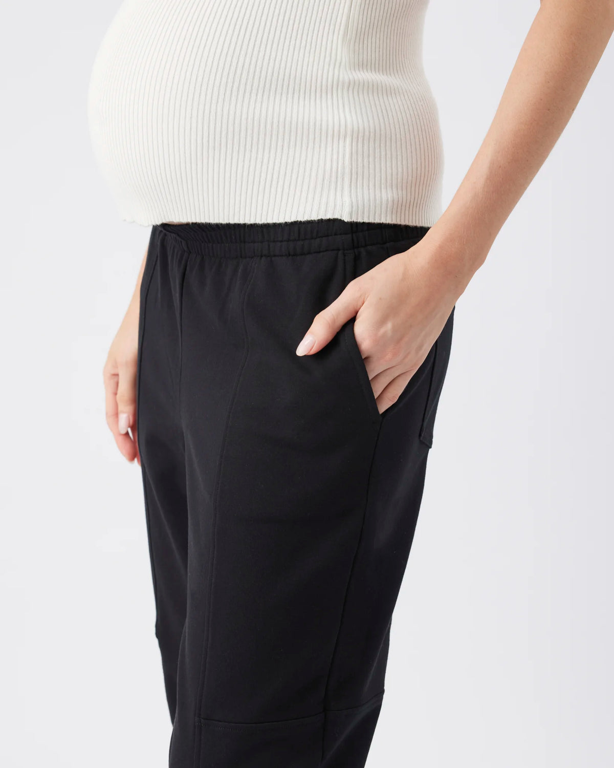 Black maternity pants with an elastic waistband and side pockets, shown on a model wearing a ribbed white top against a light gray background.