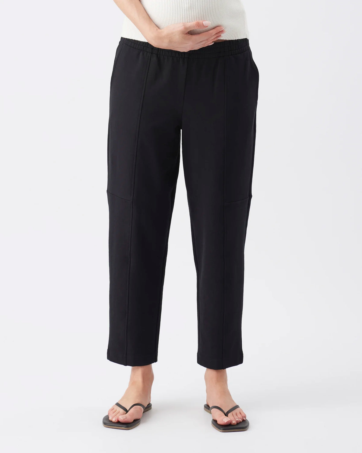 Black cropped pants with side pockets, shown on a model wearing a white ribbed top and black flip-flops against a light gray studio background.