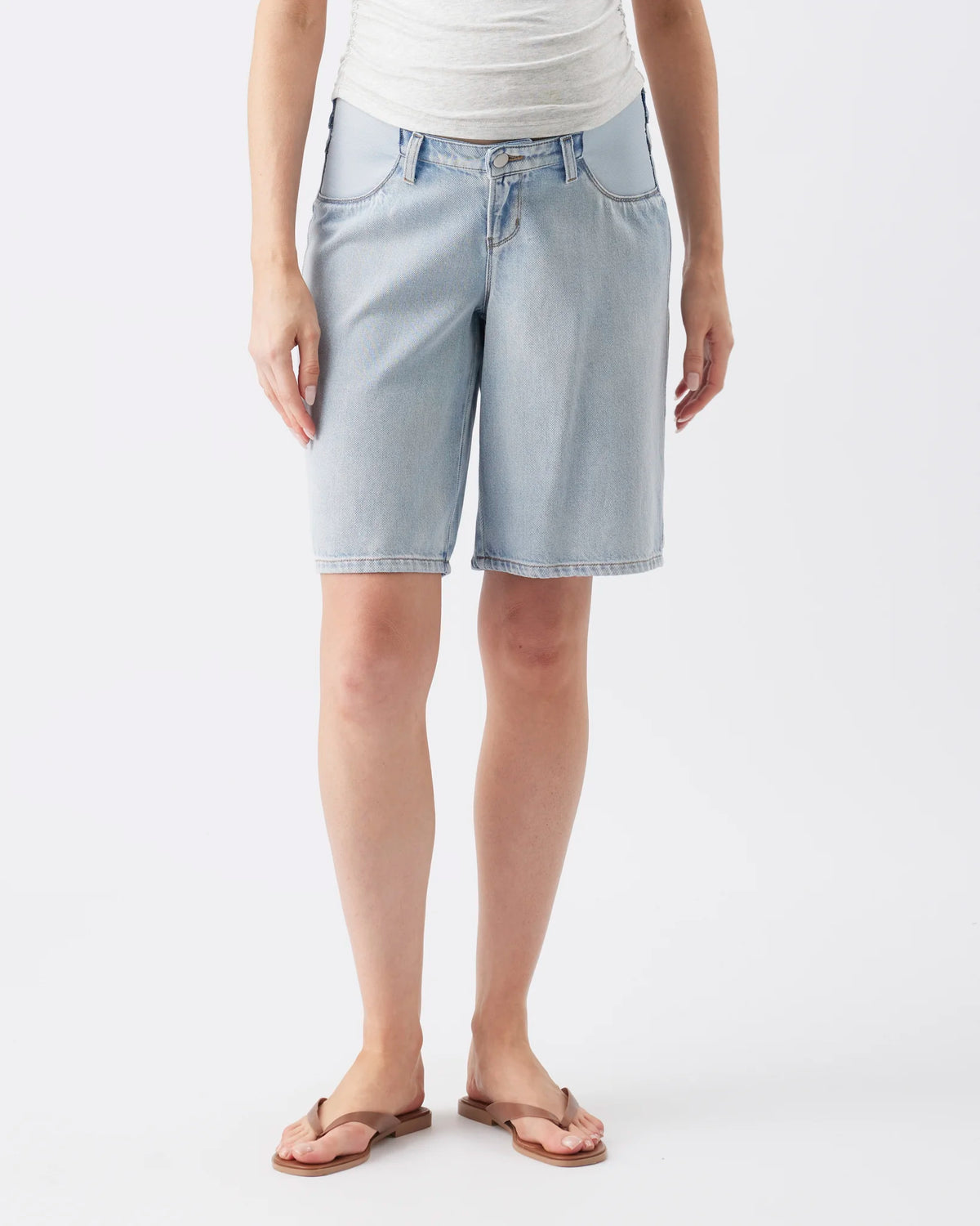 A model wearing light-wash denim shorts, a white top, and brown flip-flop sandals, shown from the waist down against a plain white studio background.