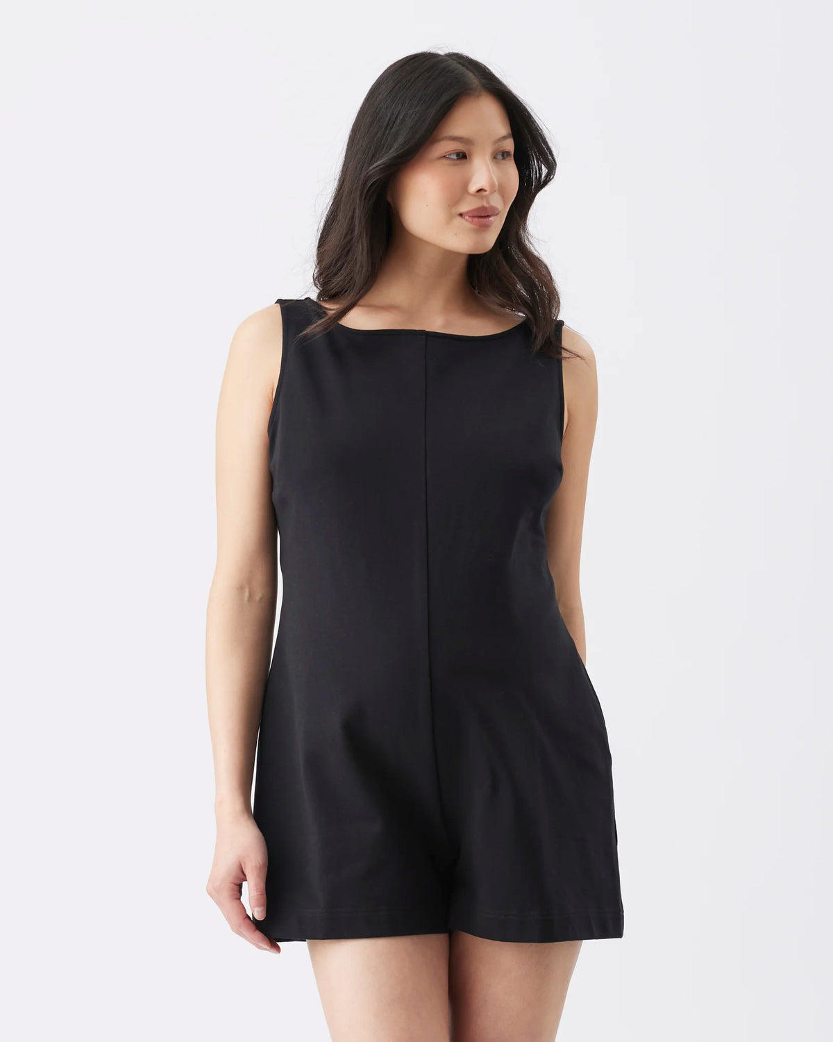 A woman modeling a sleeveless black romper with a boat neckline and front seam detail, photographed against a plain light gray studio background.