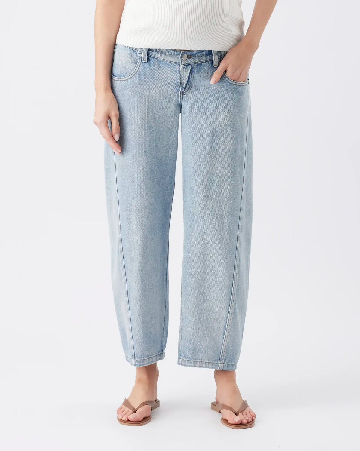 A person wearing light-wash cropped wide-leg denim jeans with a white ribbed top and flat sandals, shown against a plain light gray studio background.
