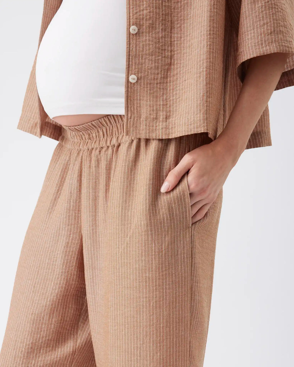 A close-up of a person wearing a matching beige textured two-piece set with a short-sleeve button-front top and wide-leg pants, styled over a white top.