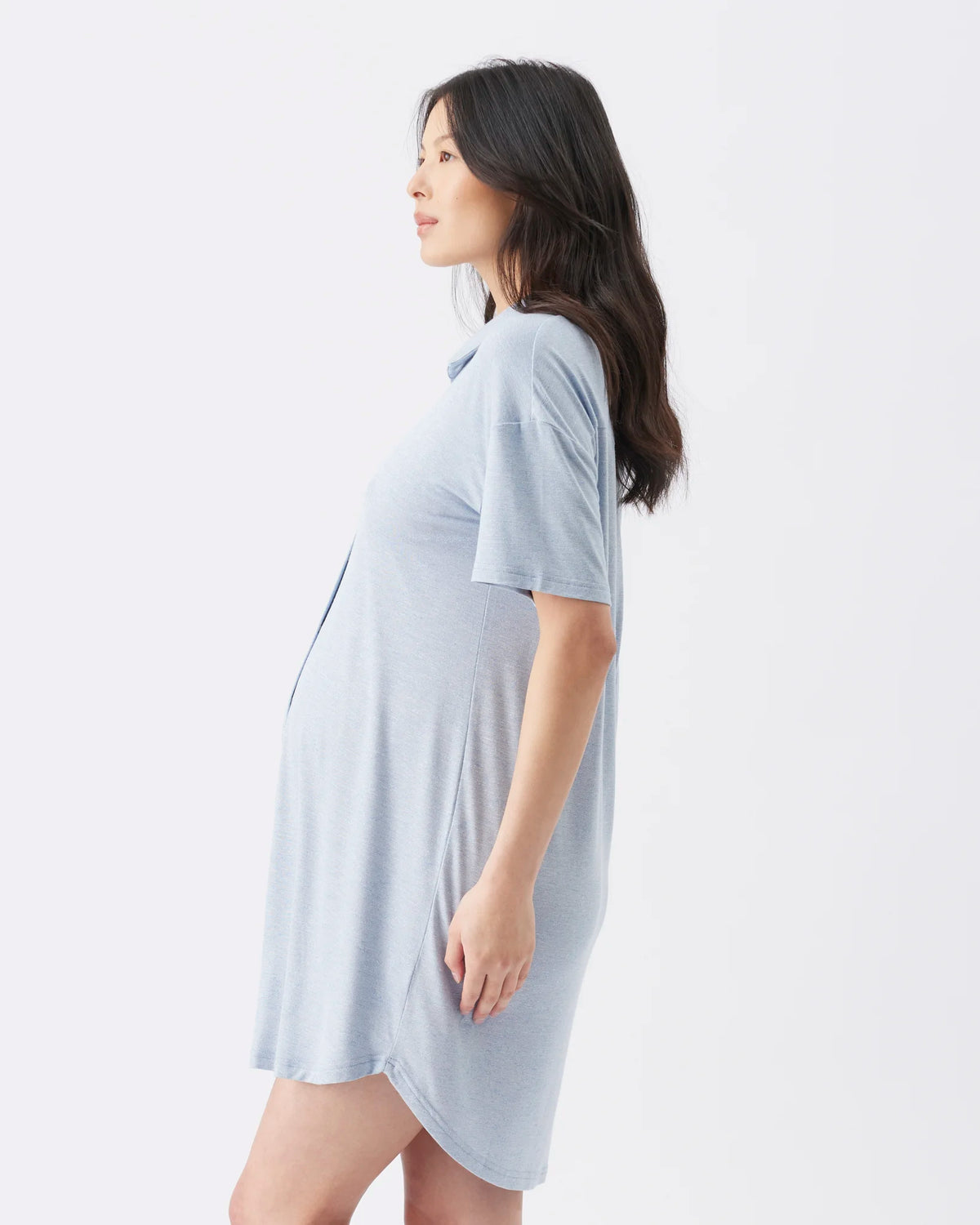 A woman in side profile wearing a light blue maternity sleep shirt dress against a plain white background.