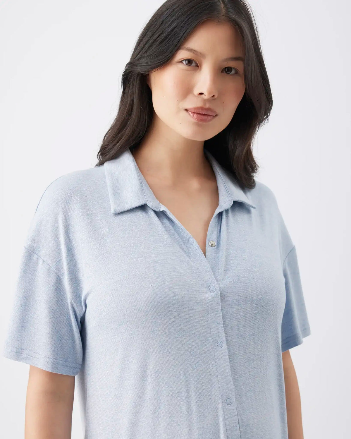 A woman wearing a light blue short-sleeve polo shirt, photographed against a clean light gray studio background.