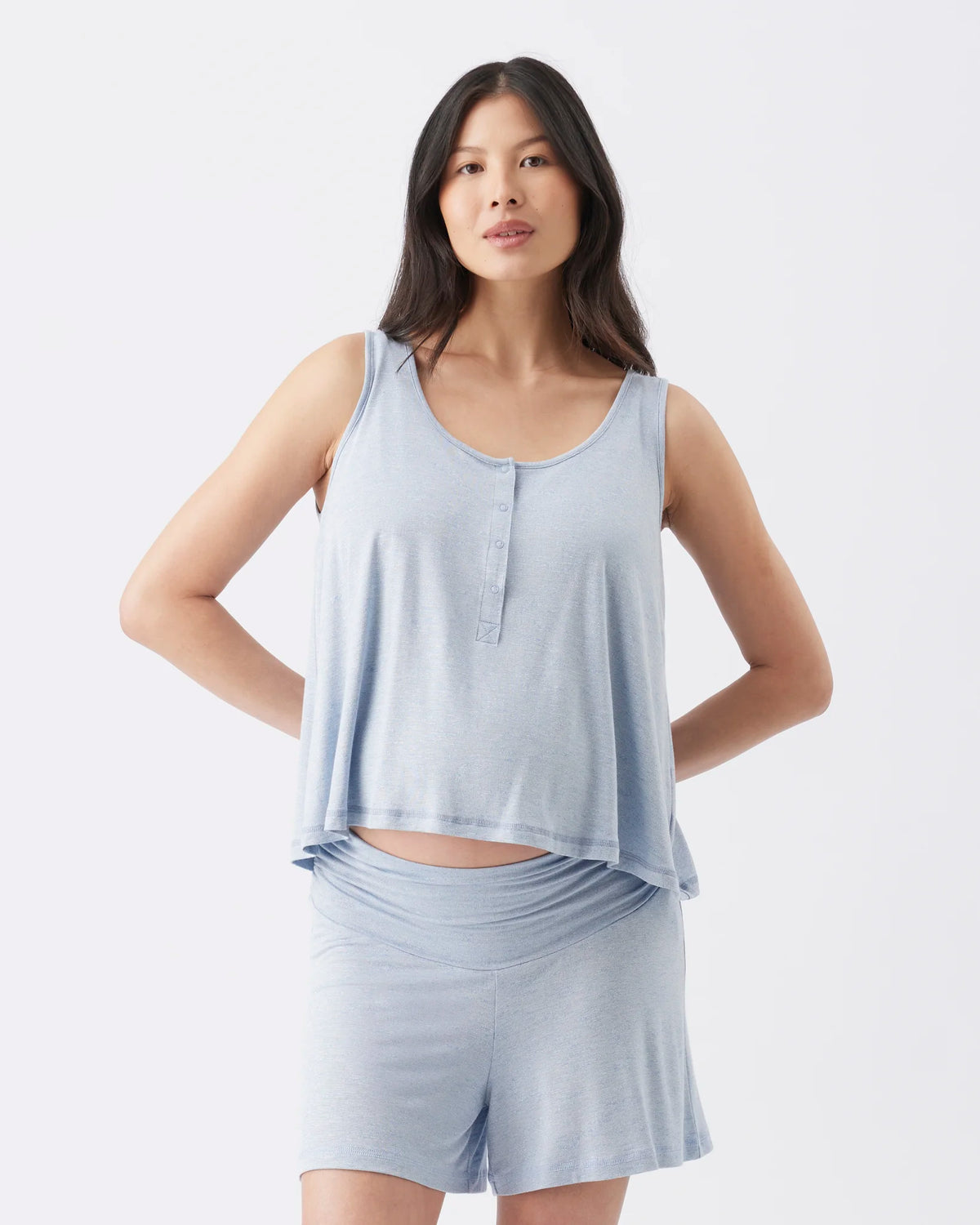 A woman modeling a light blue sleeveless henley top and matching shorts set against a plain white studio background.