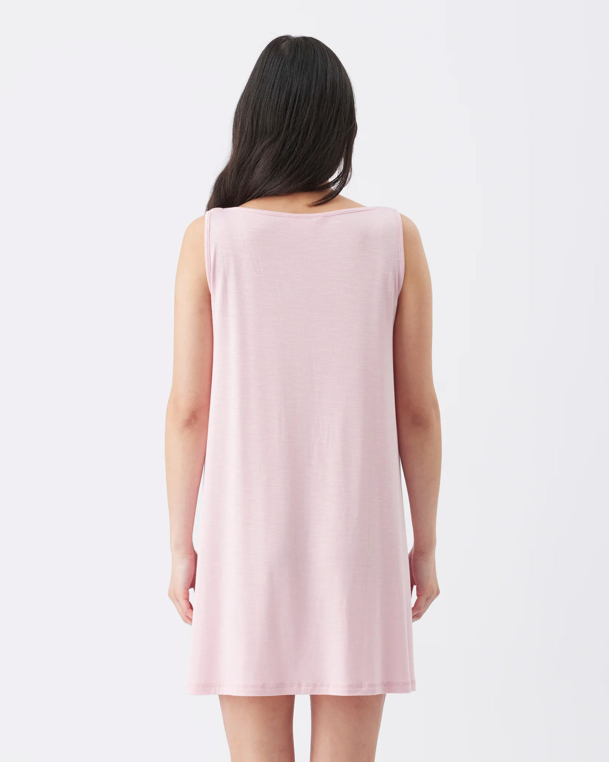 A woman viewed from behind wearing a sleeveless, light pink shift dress against a plain white studio background.