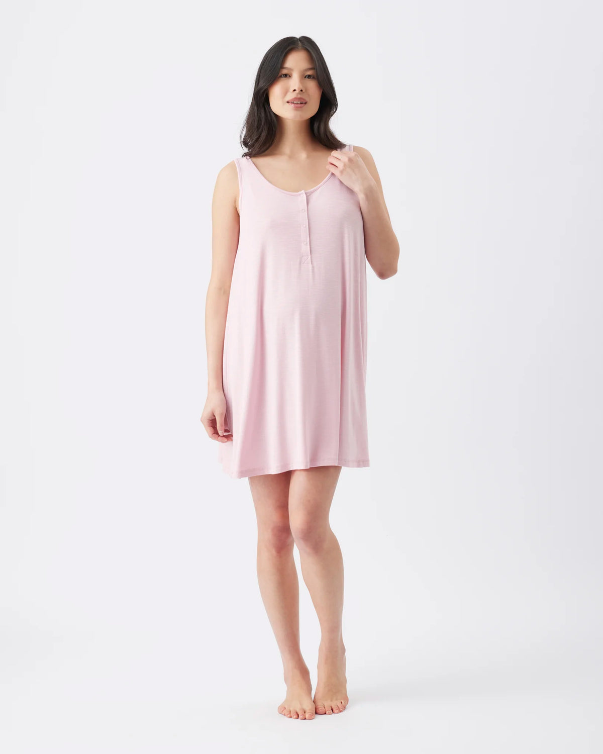 A woman modeling a light pink sleeveless nightgown or slip against a plain white studio background.