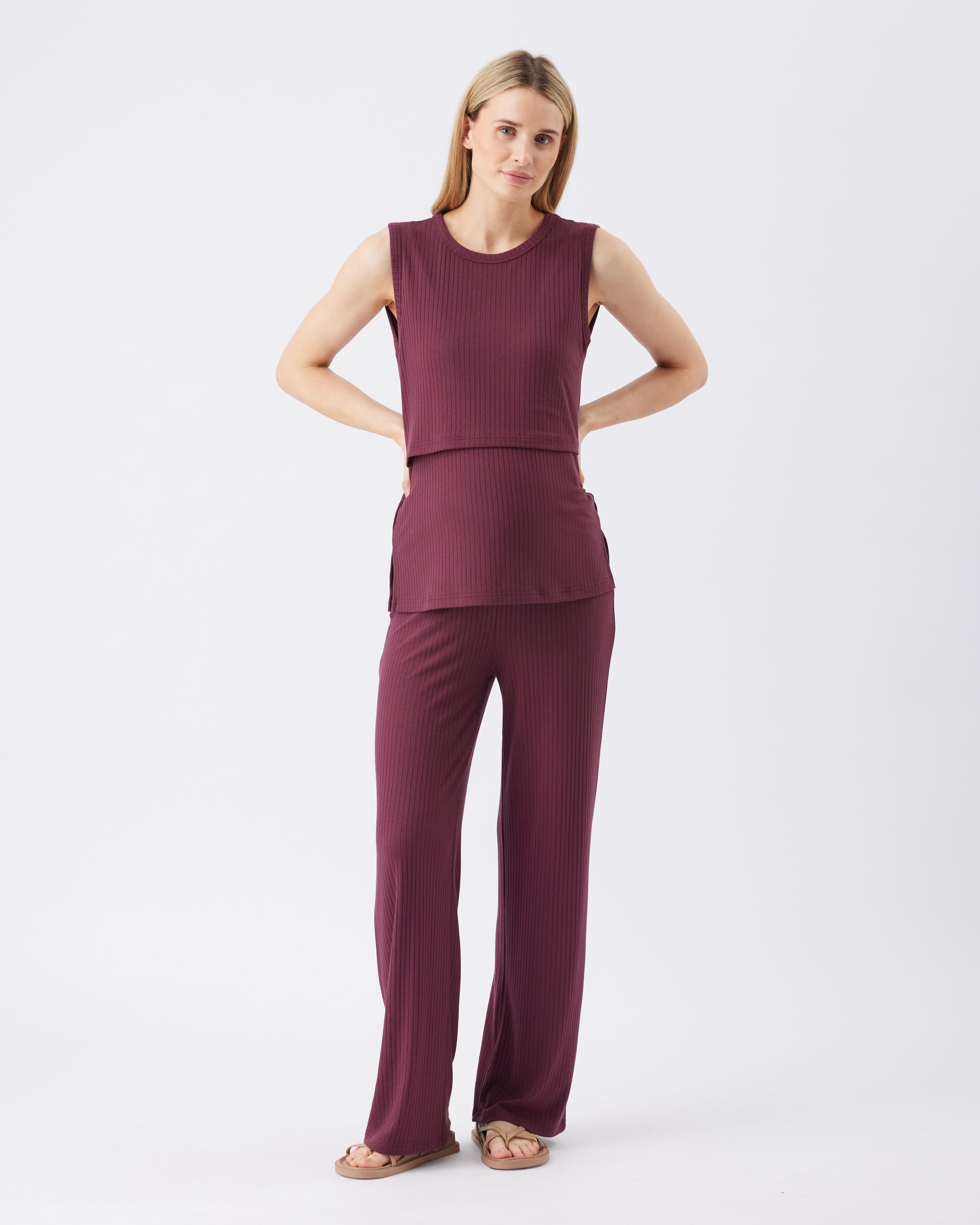 Full length shot of a woman wearing a burgundy sleeveless top and pants on a white background