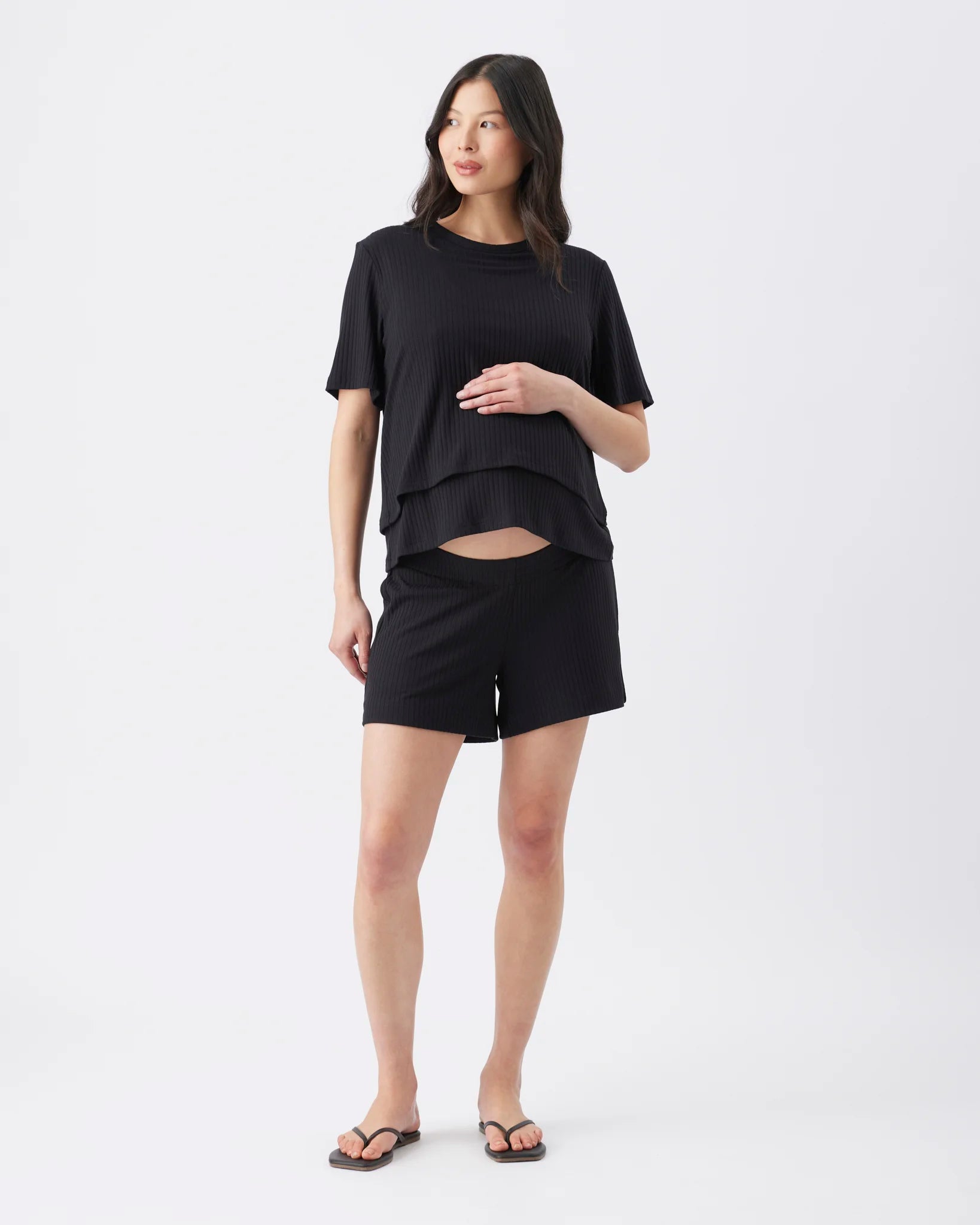 A woman modeling a black short-sleeve layered t-shirt and matching black shorts against a plain white studio background.