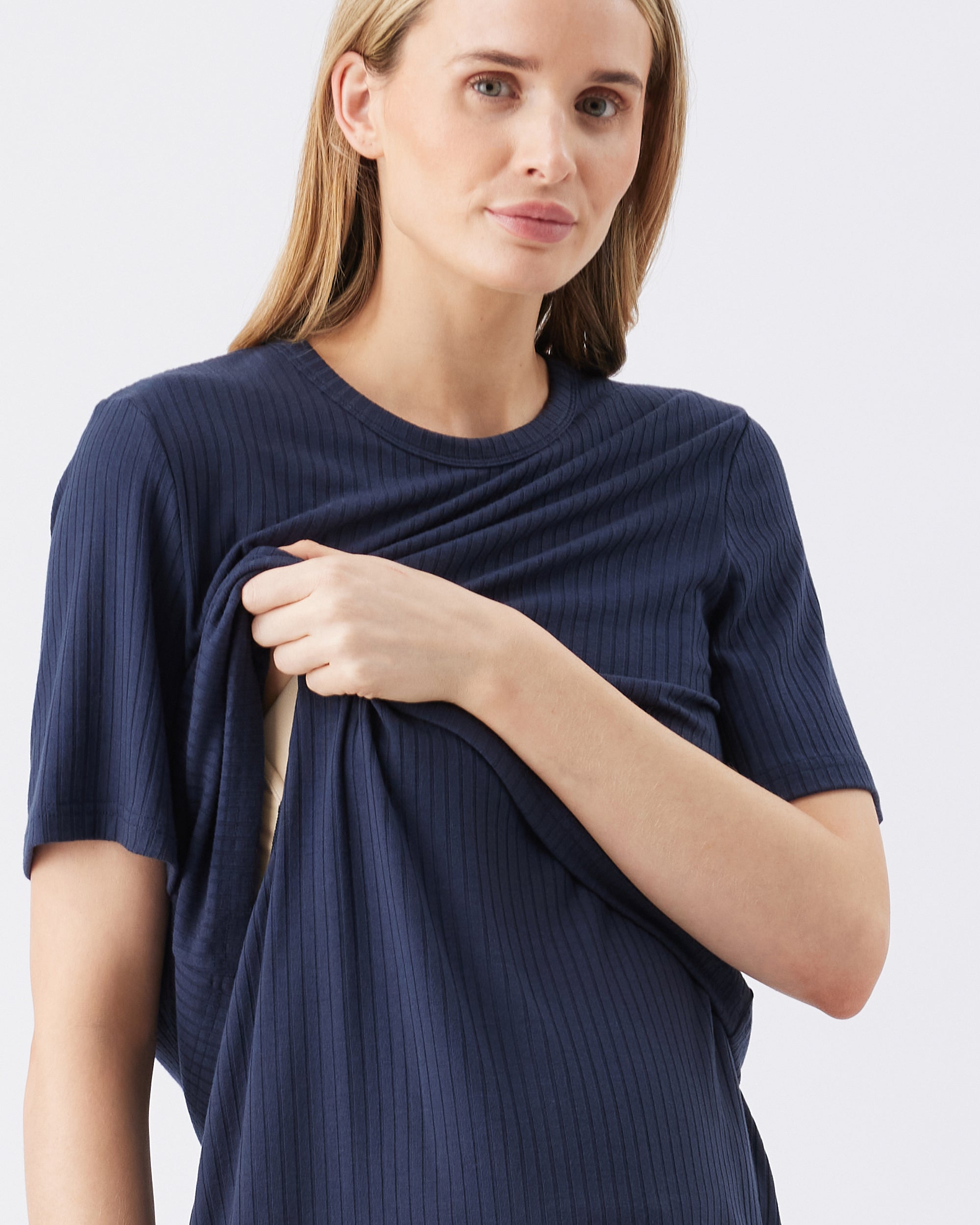 Woman showing the nursing access of a navy blue ribbed t-shirt against a light gray background