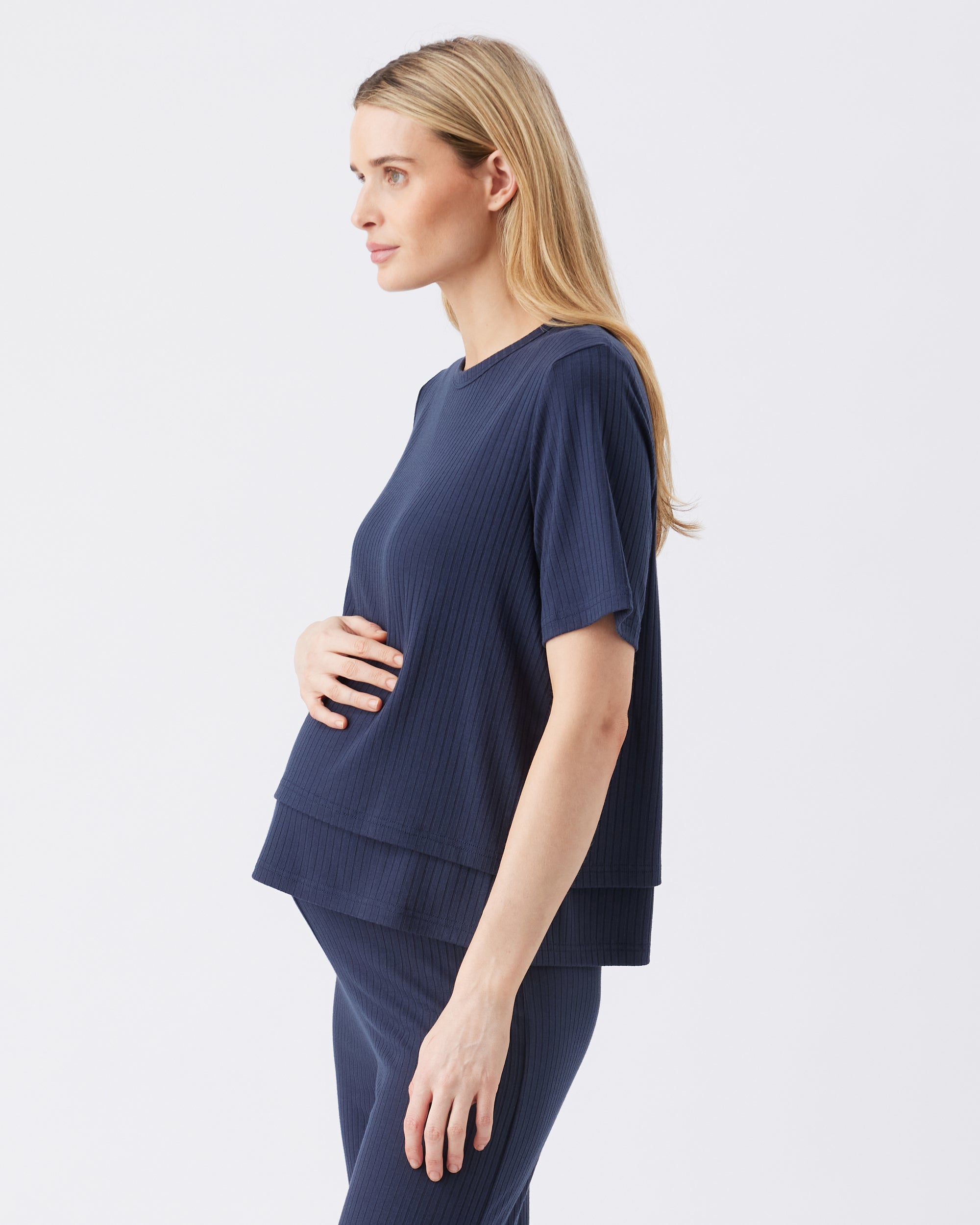 Side view of a pregnant woman wearing a navy blue outfit on a white background