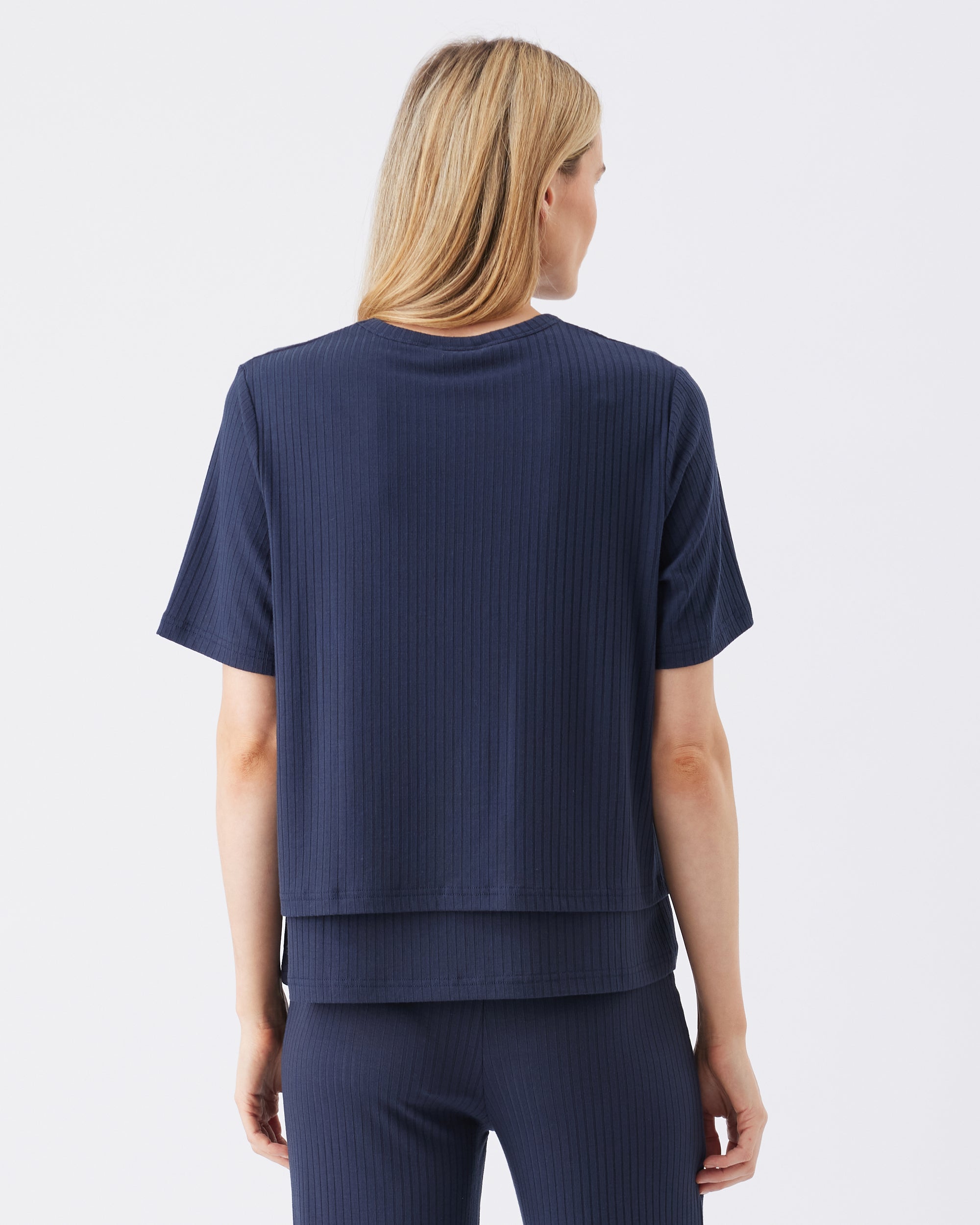 Back view of a woman wearing a navy blue ribbed t-shirt and pants on a white background