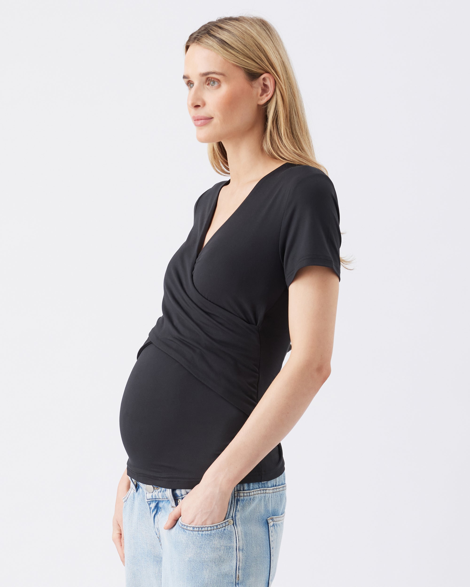 Side view of a pregnant woman wearing a black top and light blue jeans on a white background