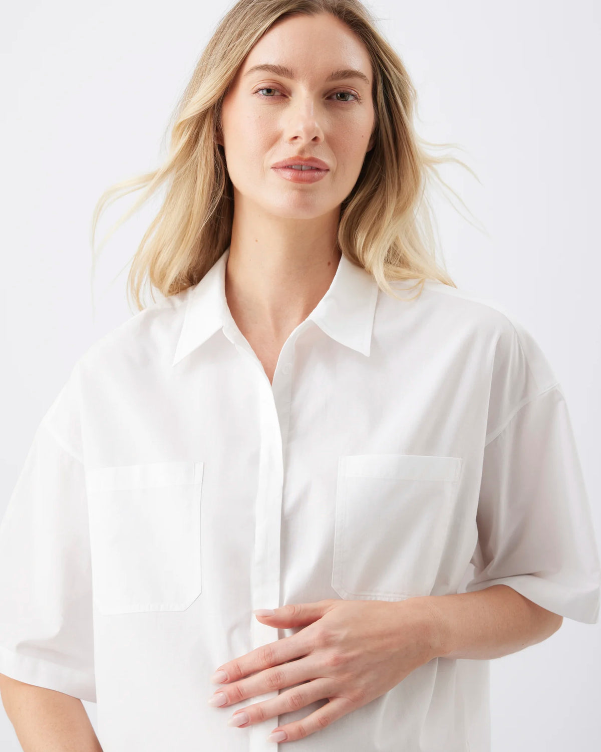 A woman wearing a white short-sleeve button-up shirt with two chest pockets, photographed against a clean white studio background.