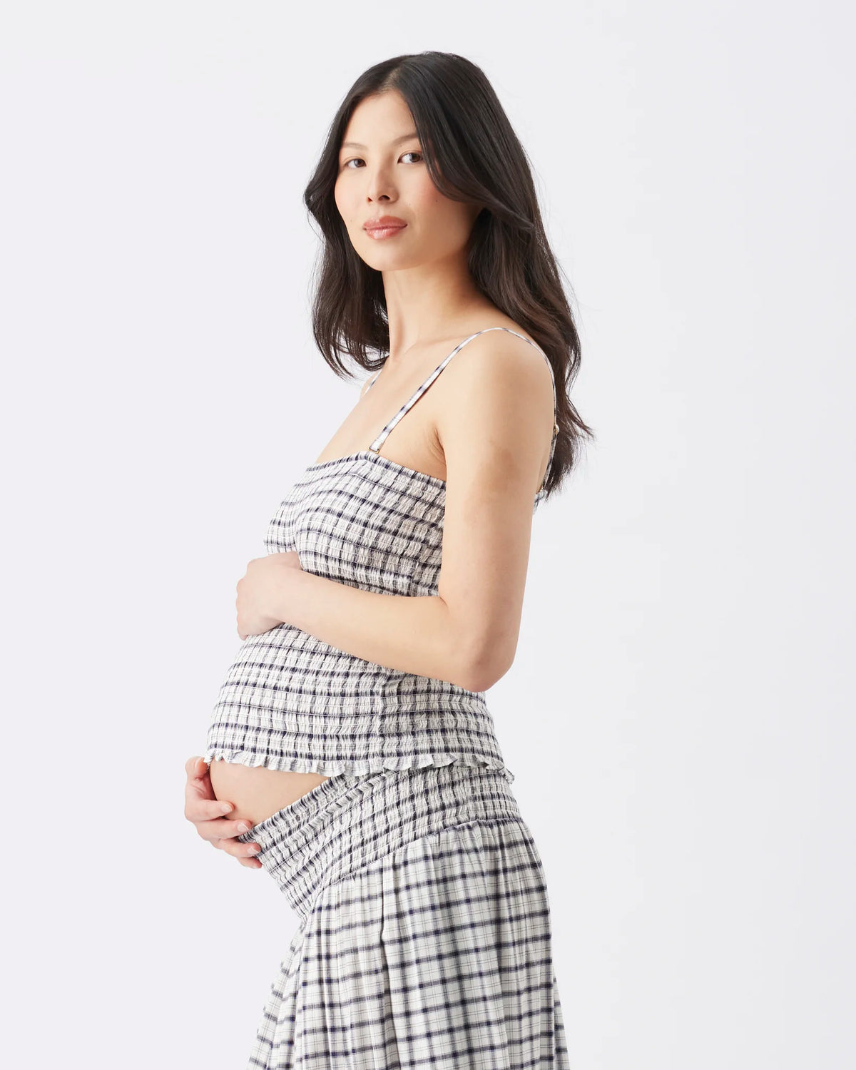 A pregnant woman wearing a matching black and white checkered strapless top and high-waisted skirt, standing against a plain white studio background.