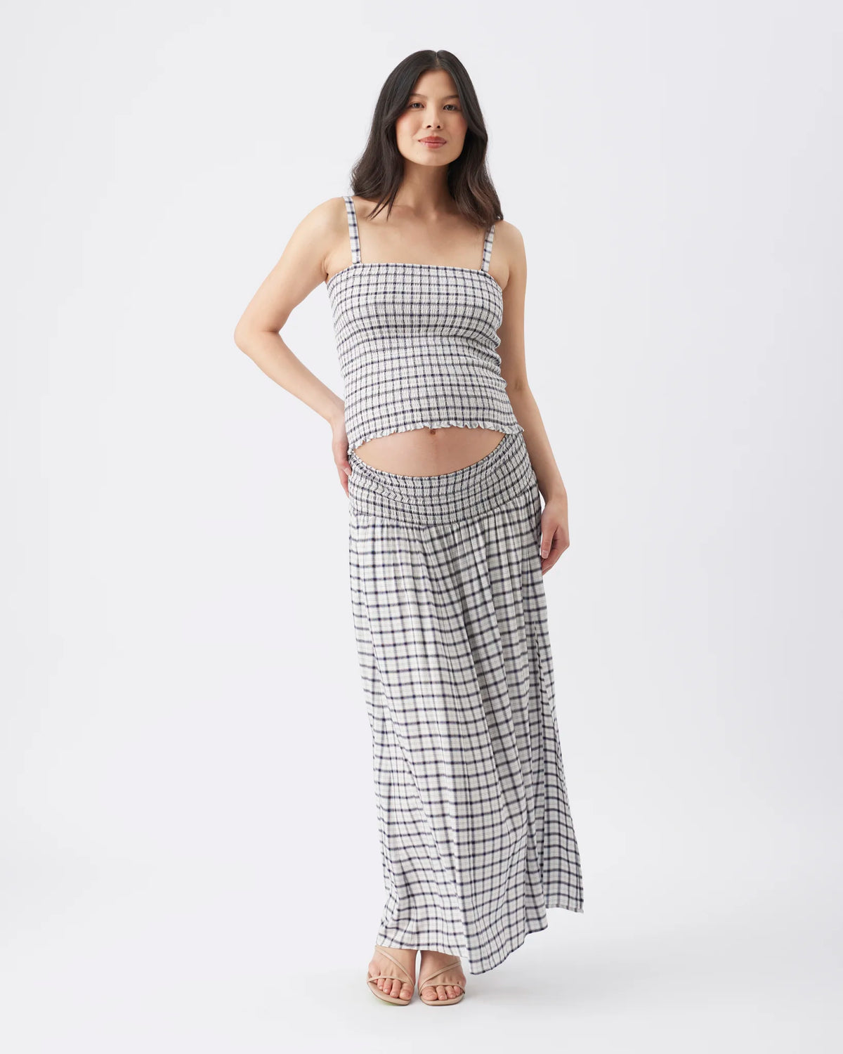 A woman modeling a matching two-piece set consisting of a black and white checkered crop top and high-waisted maxi skirt, photographed against a seamless white studio background.