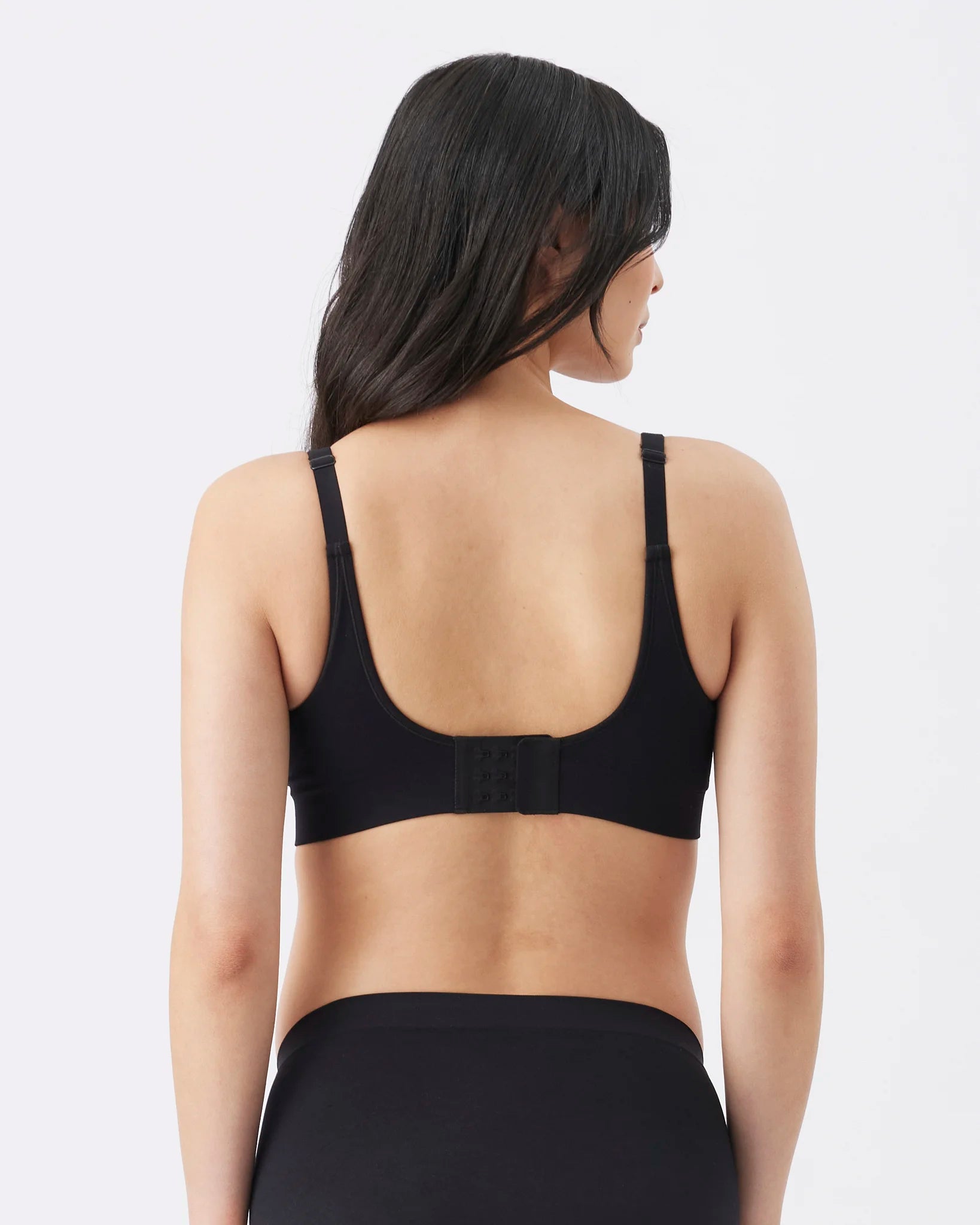 A woman shown from the back wearing a black sports bra and black bottoms against a light gray studio background.
