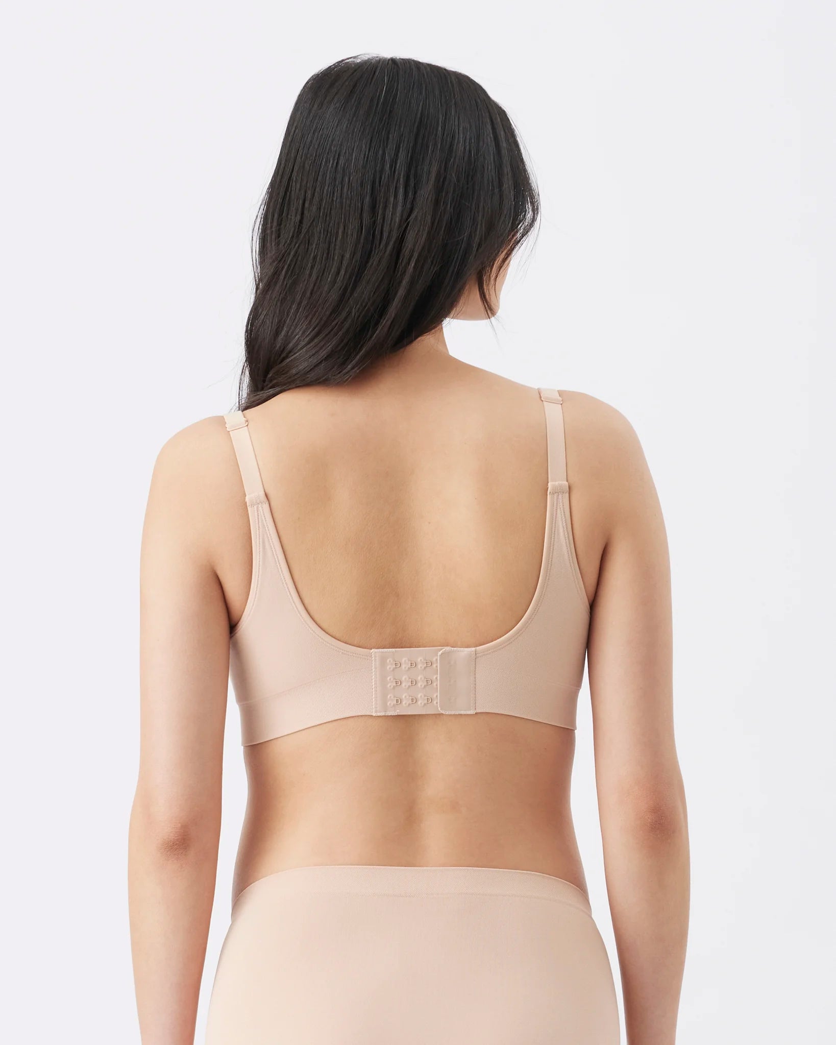 Rear view of a model wearing a beige wireless bra and matching high-waisted briefs against a light gray studio background.