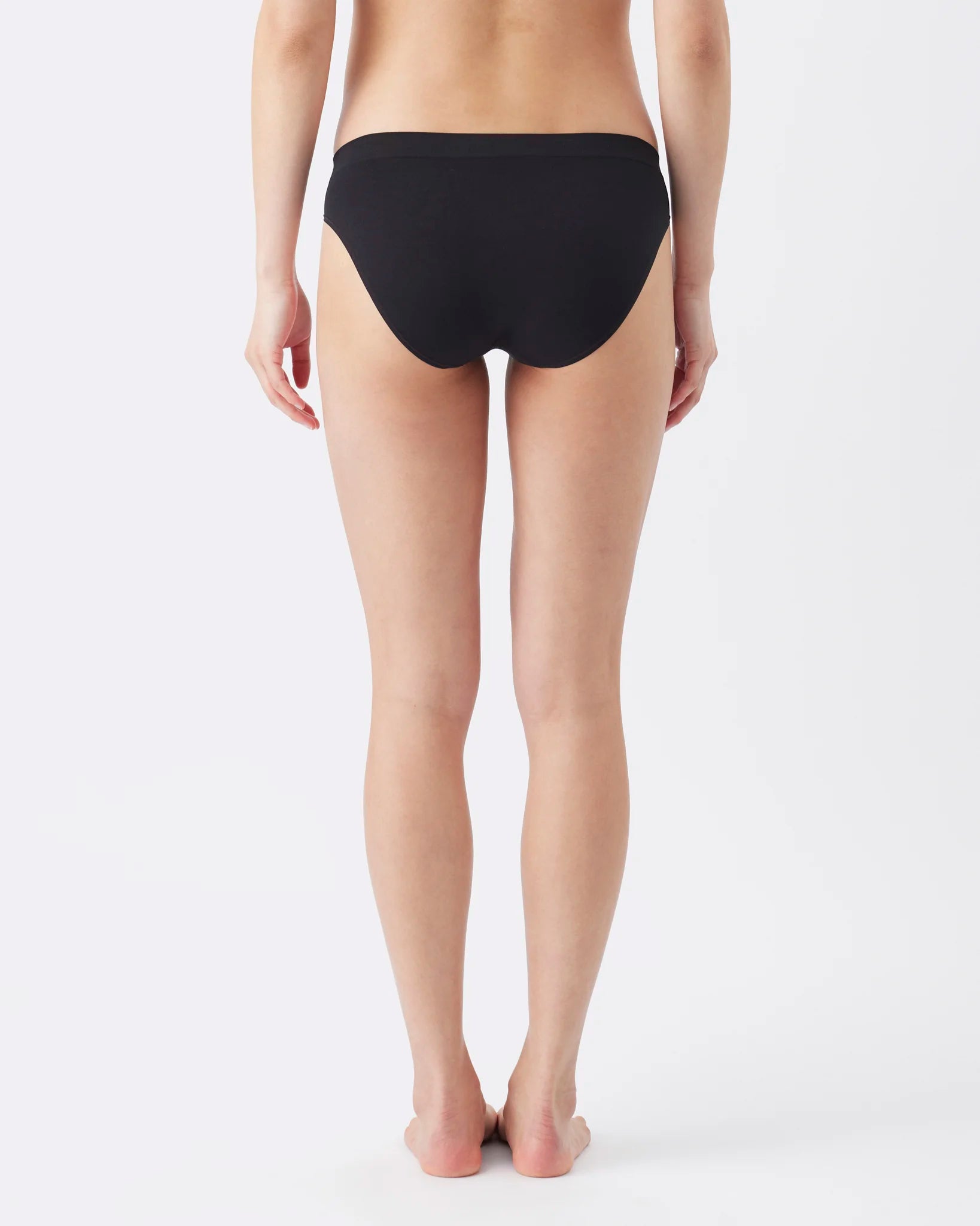 Rear view of a model wearing black bikini bottoms against a clean white studio background.