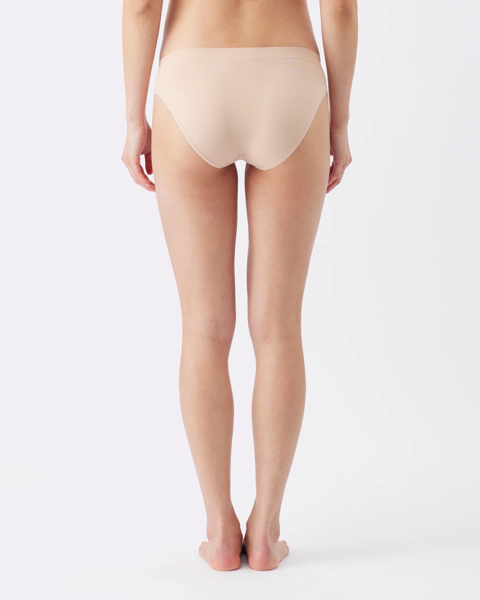Rear view of a model wearing high-waisted, seamless underwear in a light beige shade against a plain white studio background.