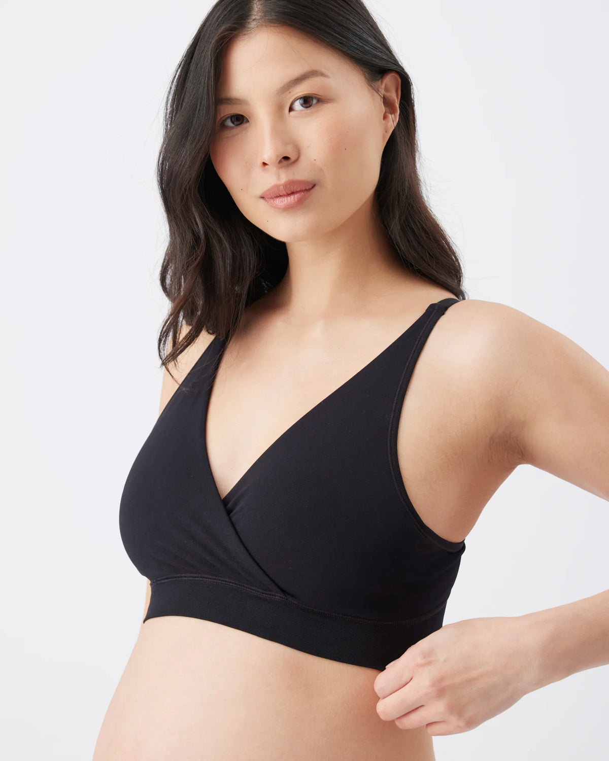 A woman wearing a black wrap-front bralette against a clean light gray studio background.