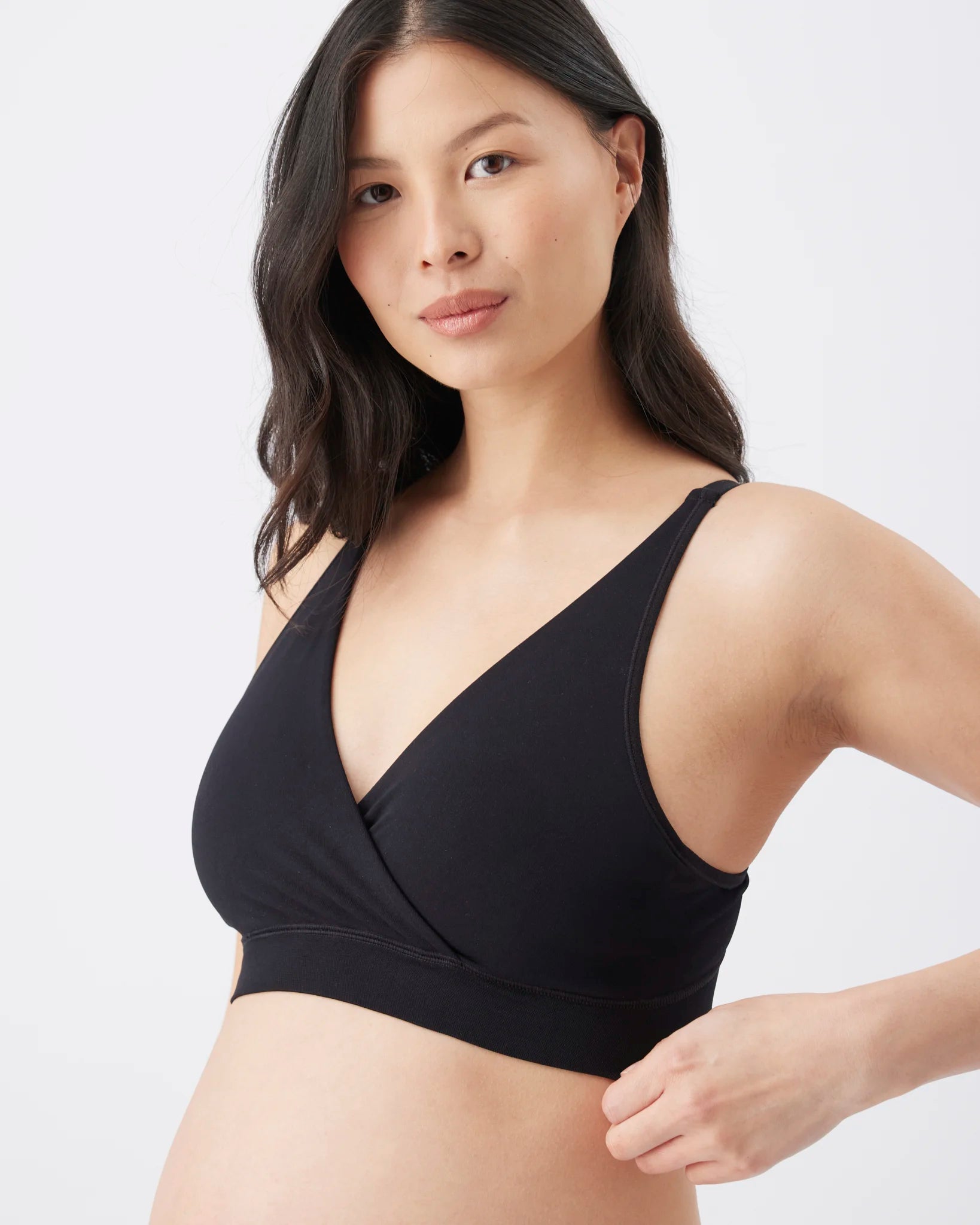 A woman wearing a black wrap-front bralette against a clean light gray studio background.