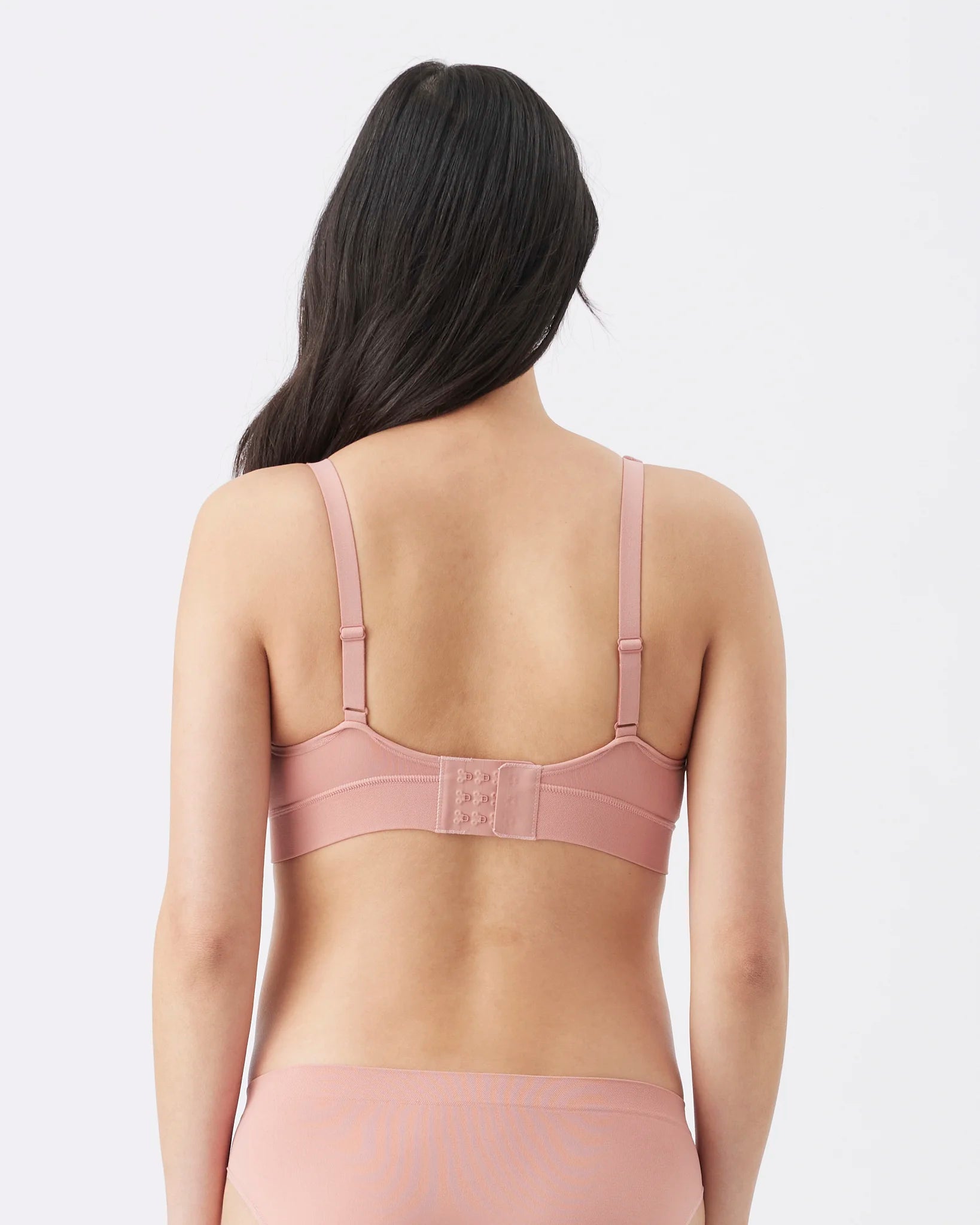A woman shown from the back wearing a dusty pink seamless bra and matching underwear against a light gray studio background.