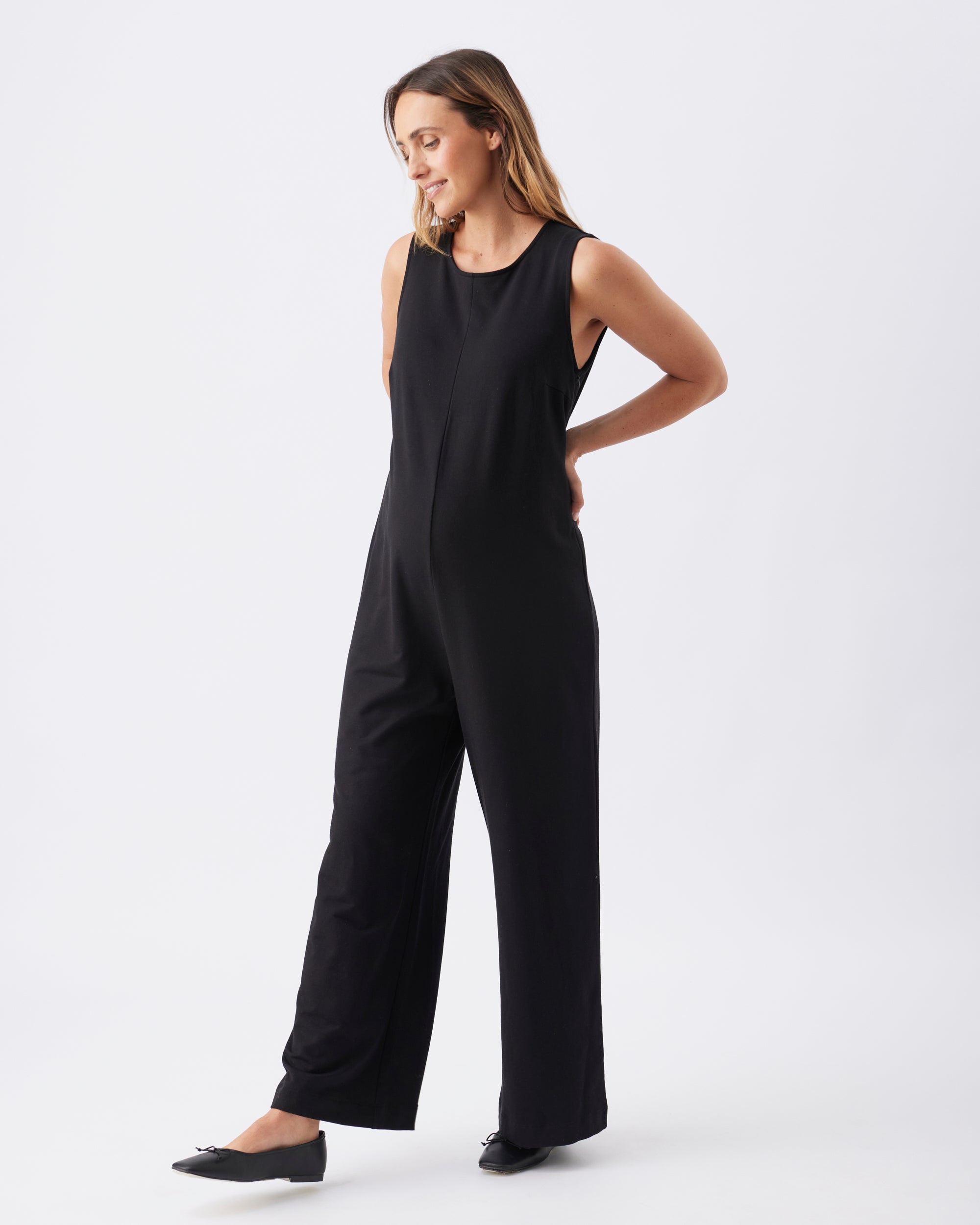 Full length side view of a pregnant woman wearing a straight leg black jumpsuit.