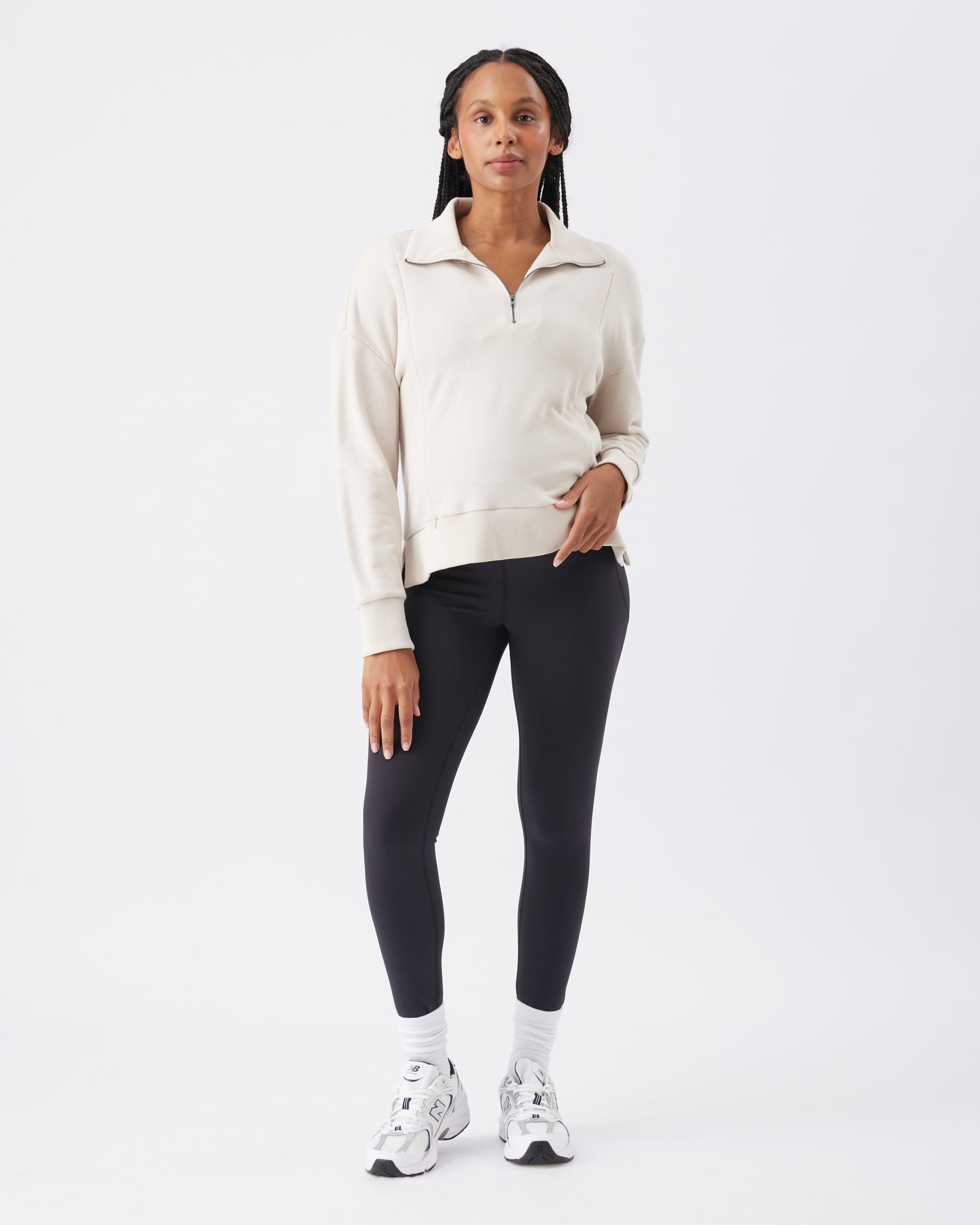Woman wearing a beige sweater and black leggings on a white background