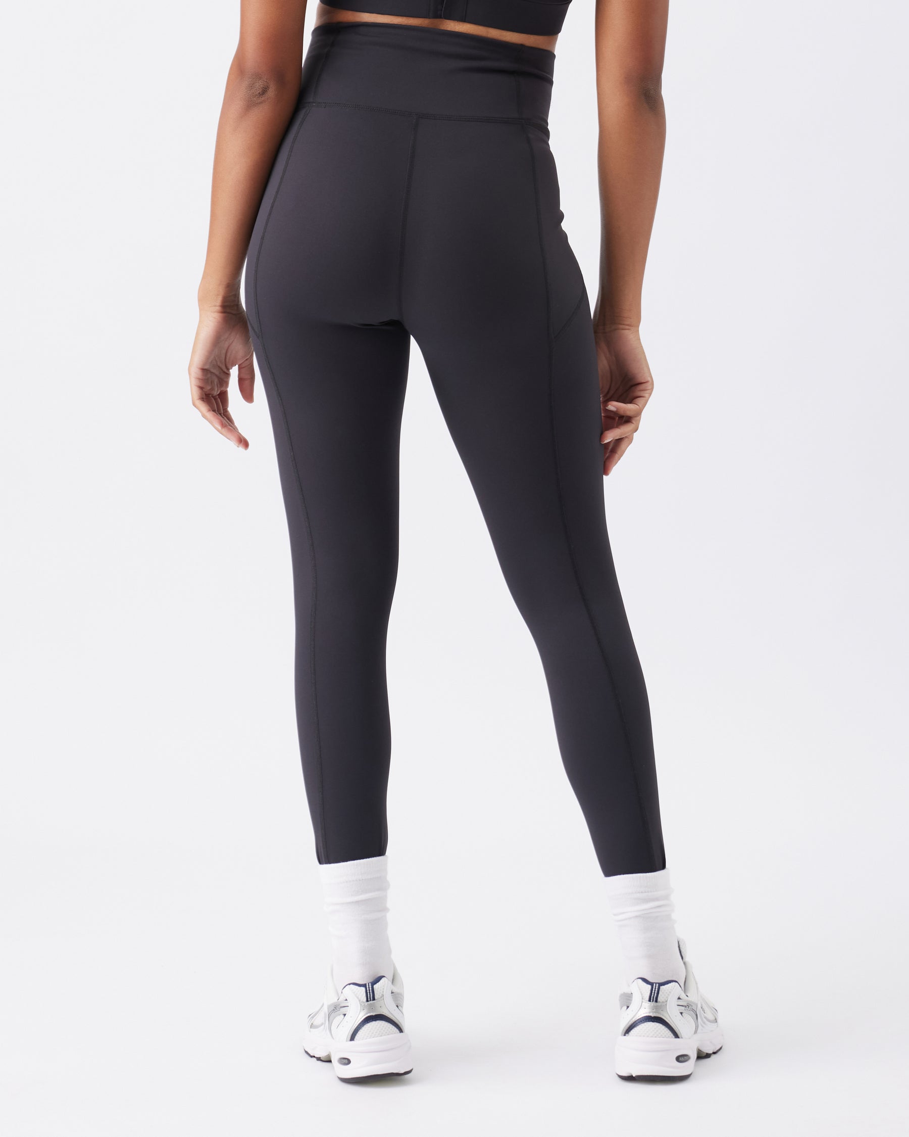 Back view of a woman wearing black leggings on a white background