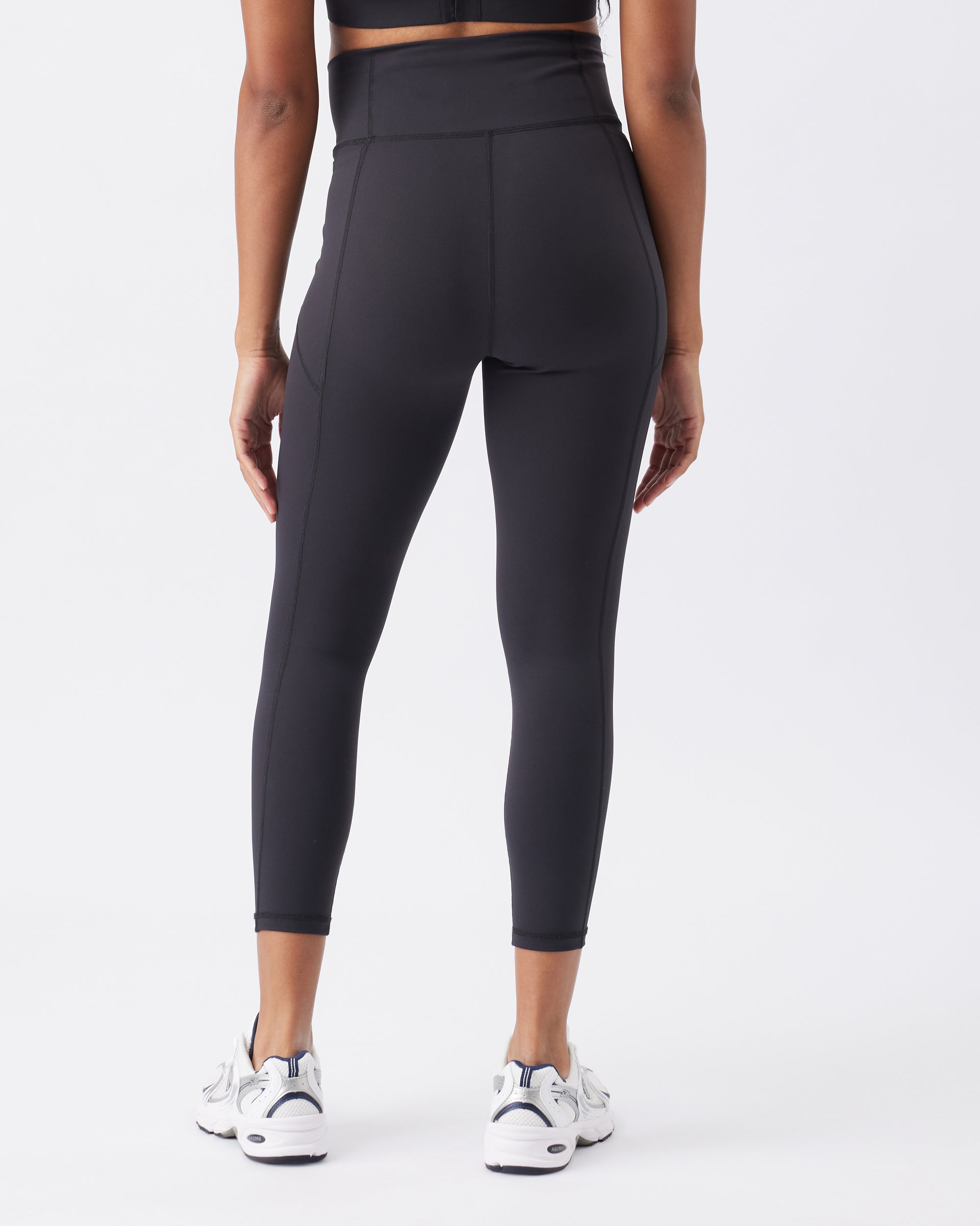 Back view of a woman wearing black high-waisted active leggings on a white background